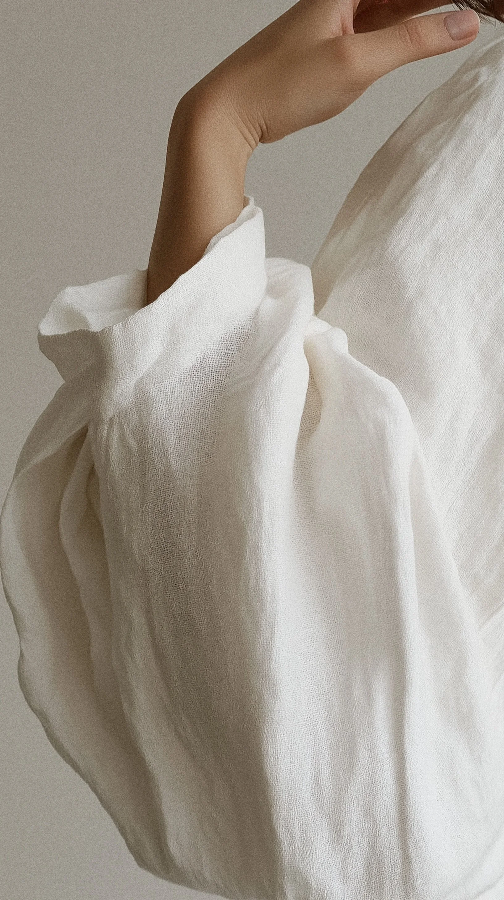 Close-up of a person's hand holding a white, textured fabric shirt against a plain background.
