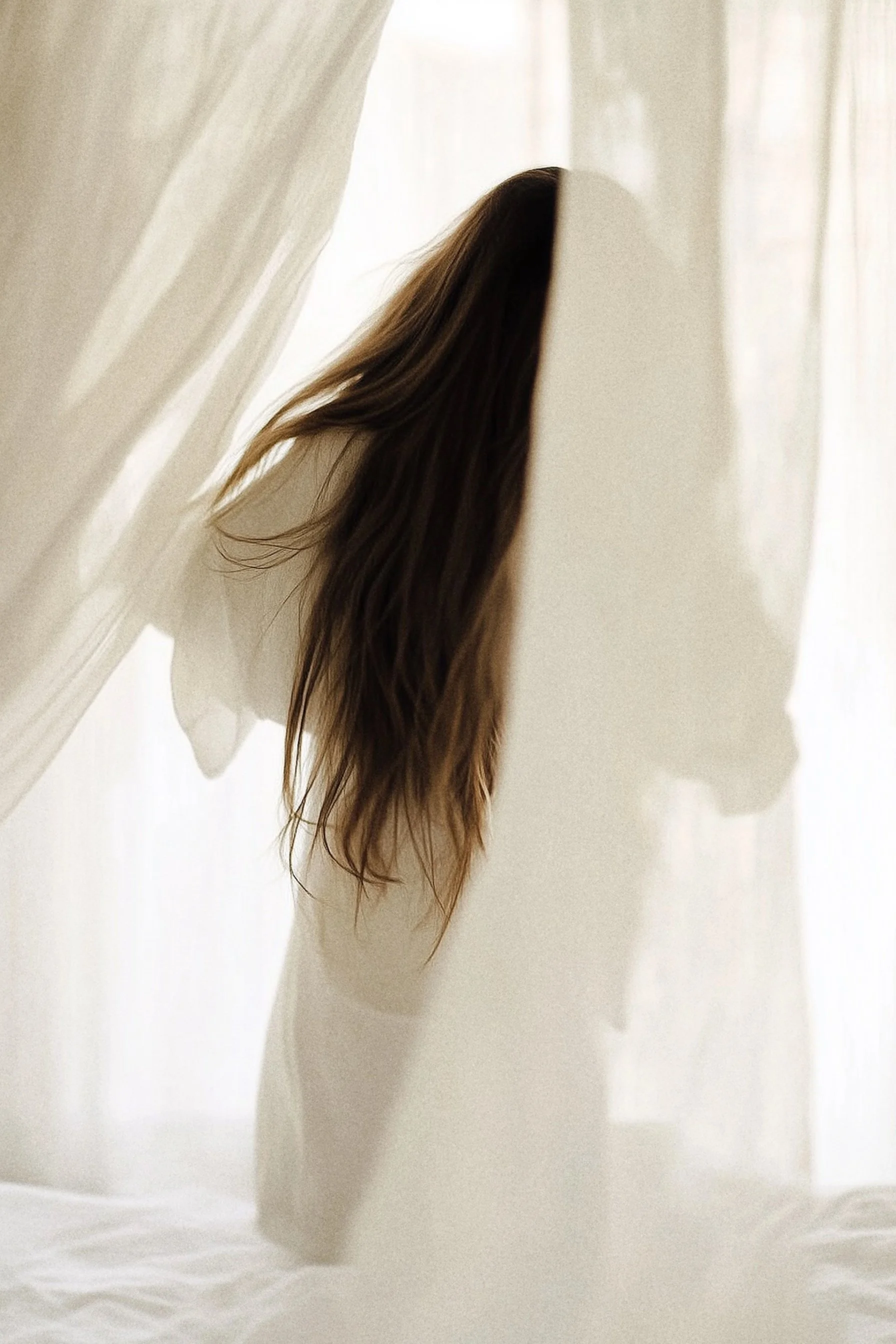 Close-up of brown hair hanging in front of a white wall or curtain.