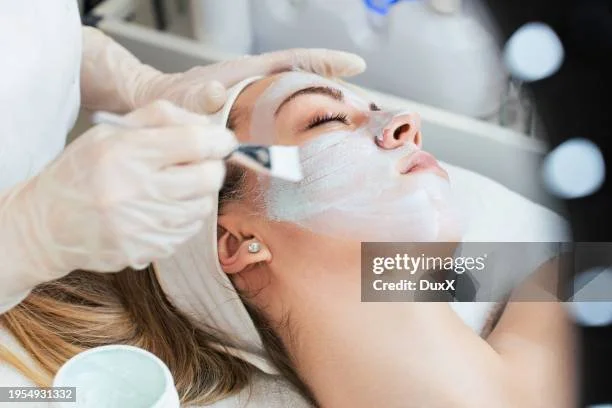 Person receiving facial treatment at a spa or clinic, with a skincare professional applying a facial mask.