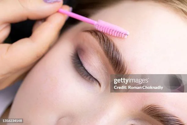 A person cleaning an eyebrow with a small pink brush.