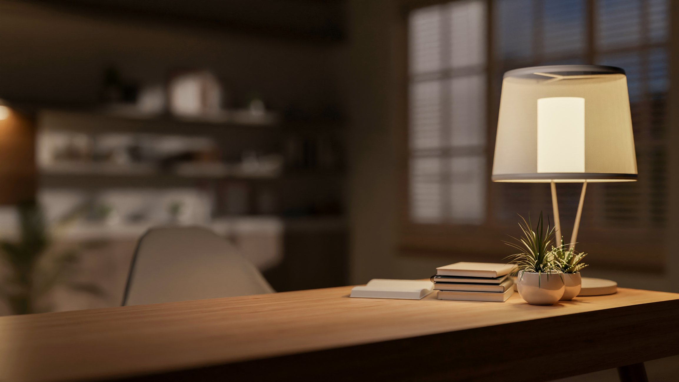 A wooden table with a small potted plant, a stack of books, and a table lamp in a cozy room with window blinds.
