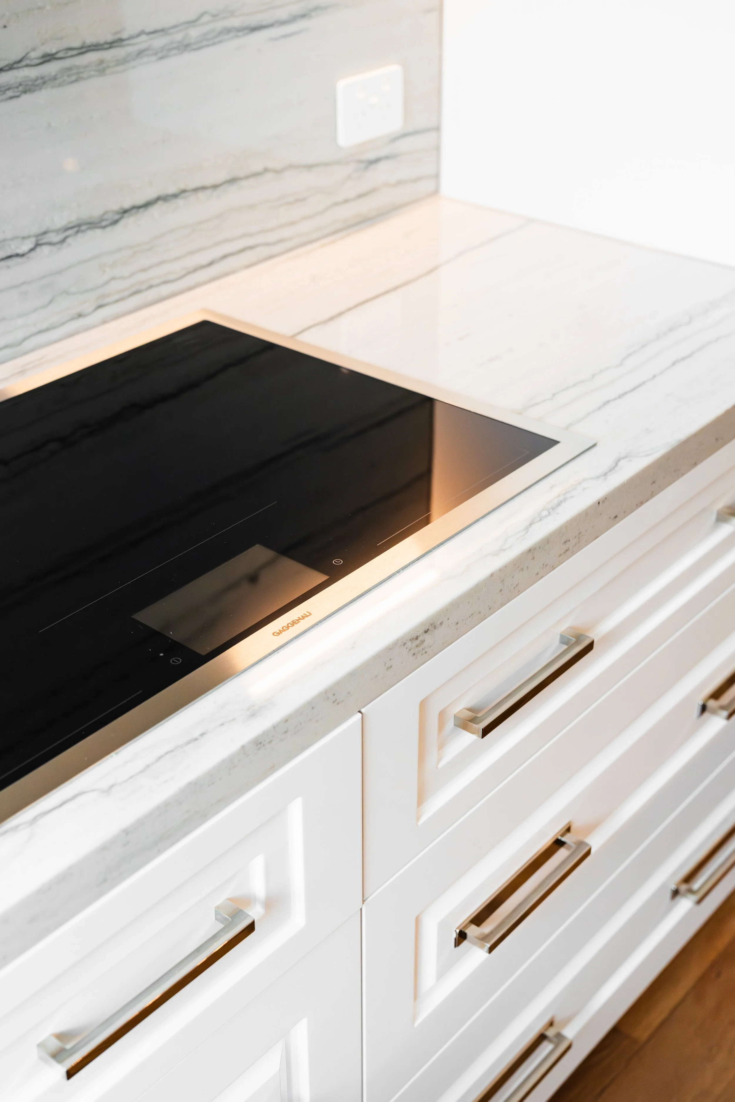 Countertop with a black electric cooktop and white marble backsplash with gray veining, alongside a white cabinet with silver handles.