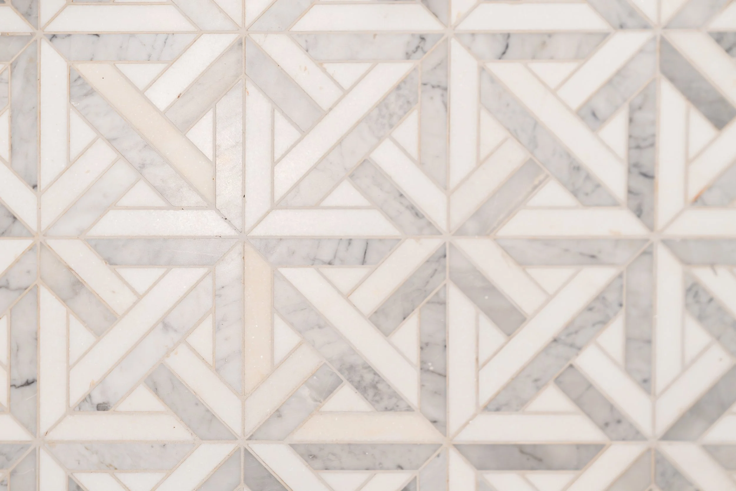 Close-up view of a white marble tile wall with geometric patterns and thin grout lines.