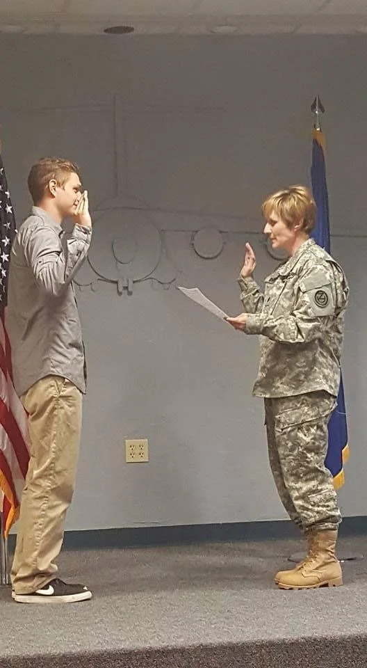 A young man taking the oath of enlistment while a female military officer in uniform administers the oath in a room with American and military flags.
