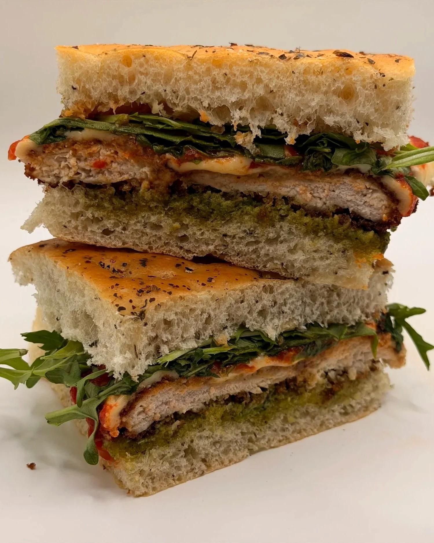 Close-up of a layered vegetable and chicken sandwich with herbs, sauce, and bread slices.