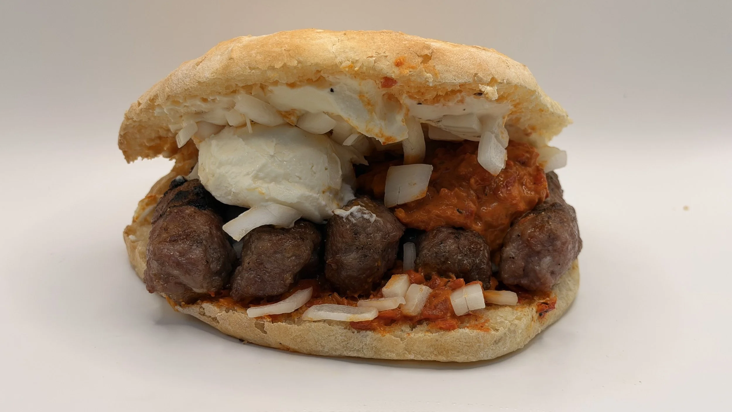 A gyro sandwich with pita bread, grilled meatballs, chopped onions, tomato sauce, shredded cabbage, and a dollop of white sauce, all on a white background.