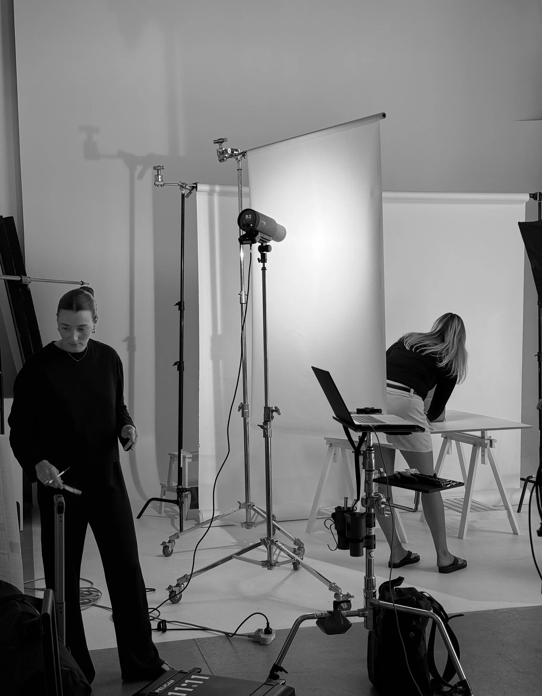 People in a photography studio setting with lighting equipment and backdrops, preparing for a photo shoot.