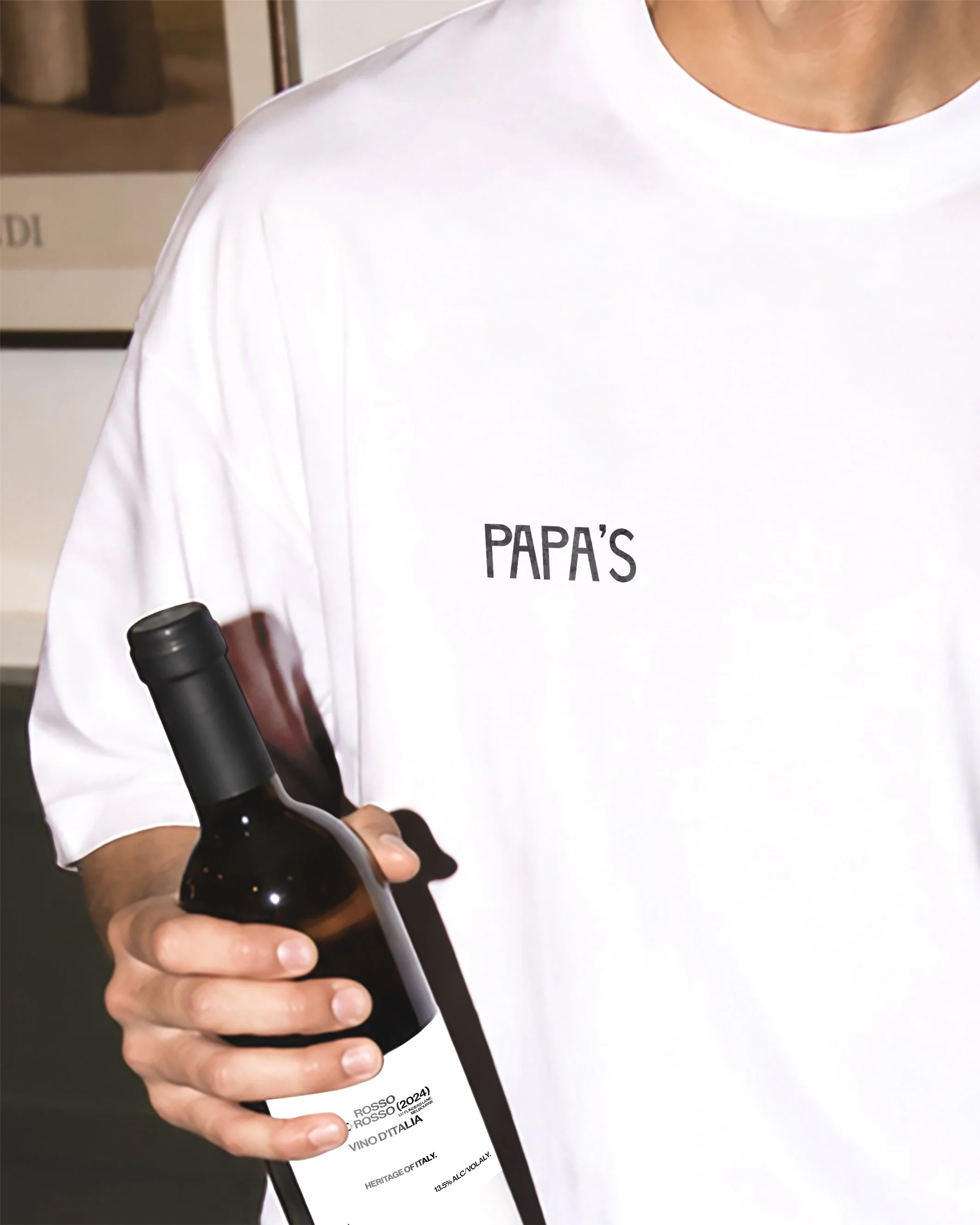 Person wearing a white shirt holding a bottle of red wine.