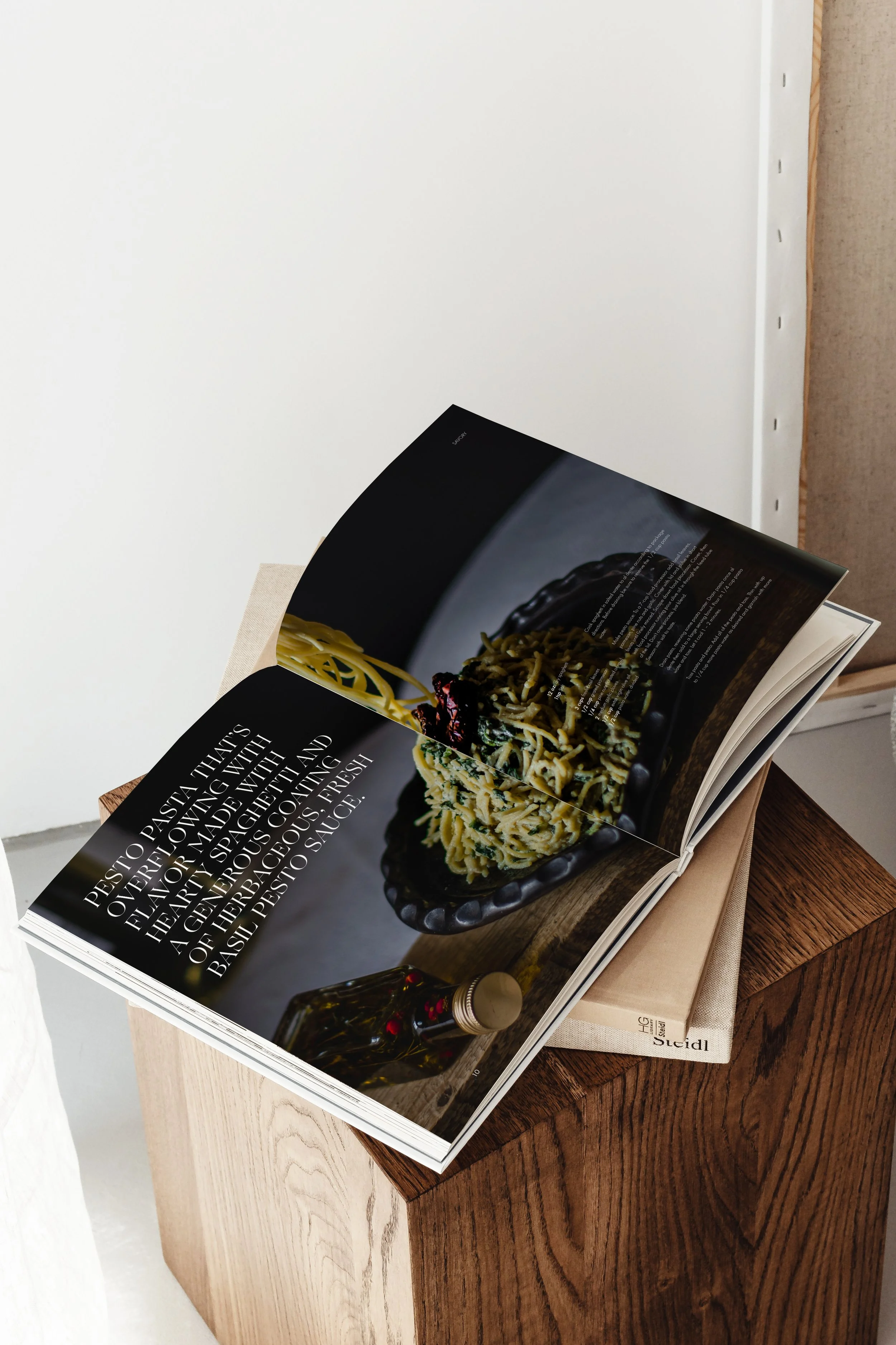 Open cookbook displaying a page with a pasta dish, placed on a wooden table against a plain white wall.