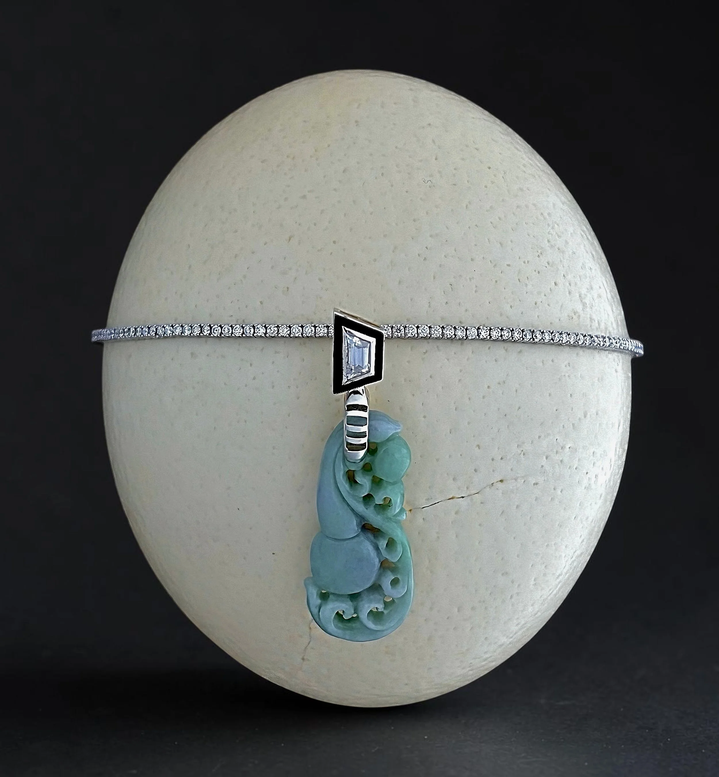 Close-up photo of a decorated Easter egg with a pearl-like band, a framed mirror, and a blue-green ribbon flower against a black background.