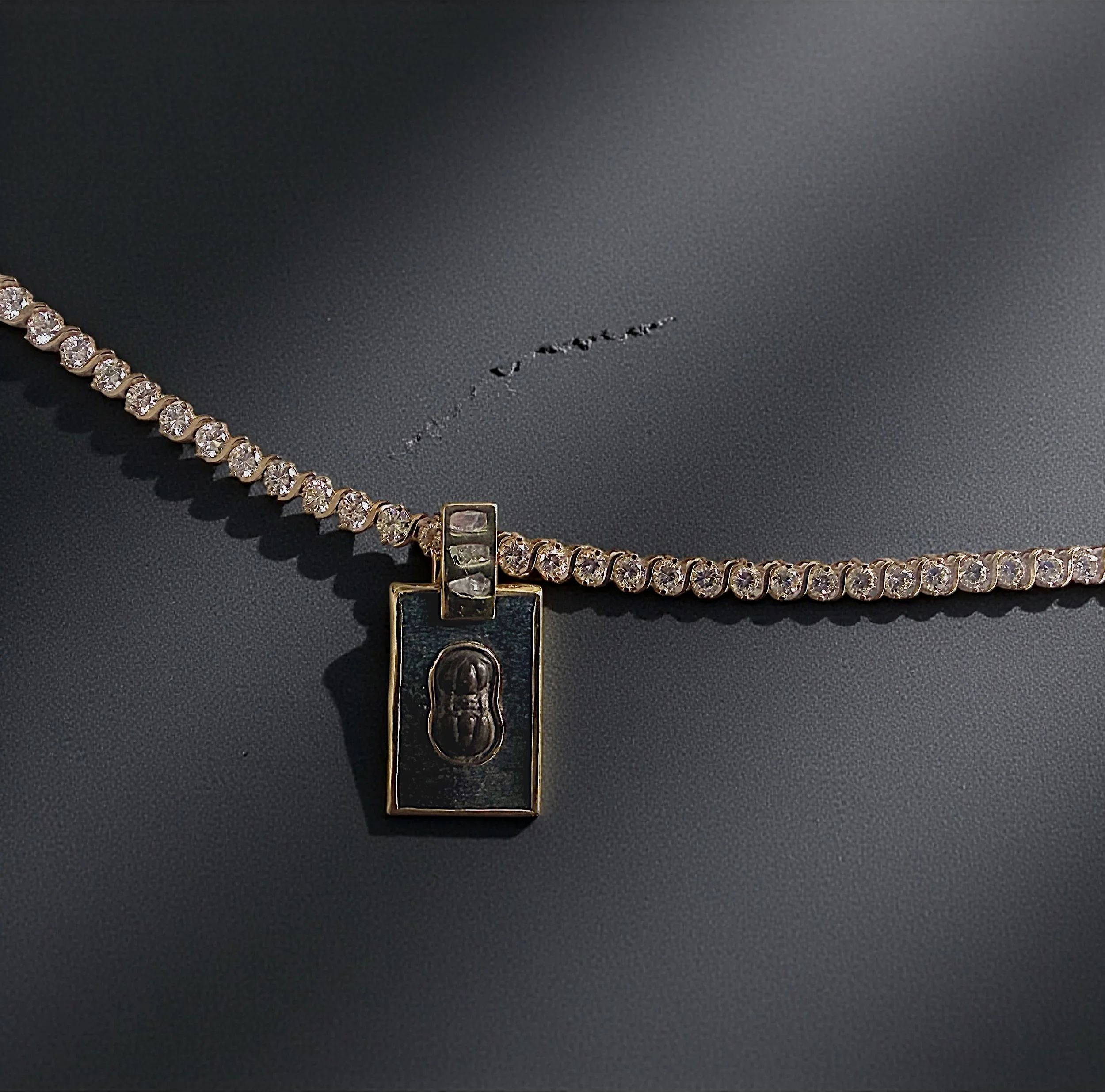 A gold chain necklace with round-cut diamonds laid out on a dark, textured surface with a groove in the background.