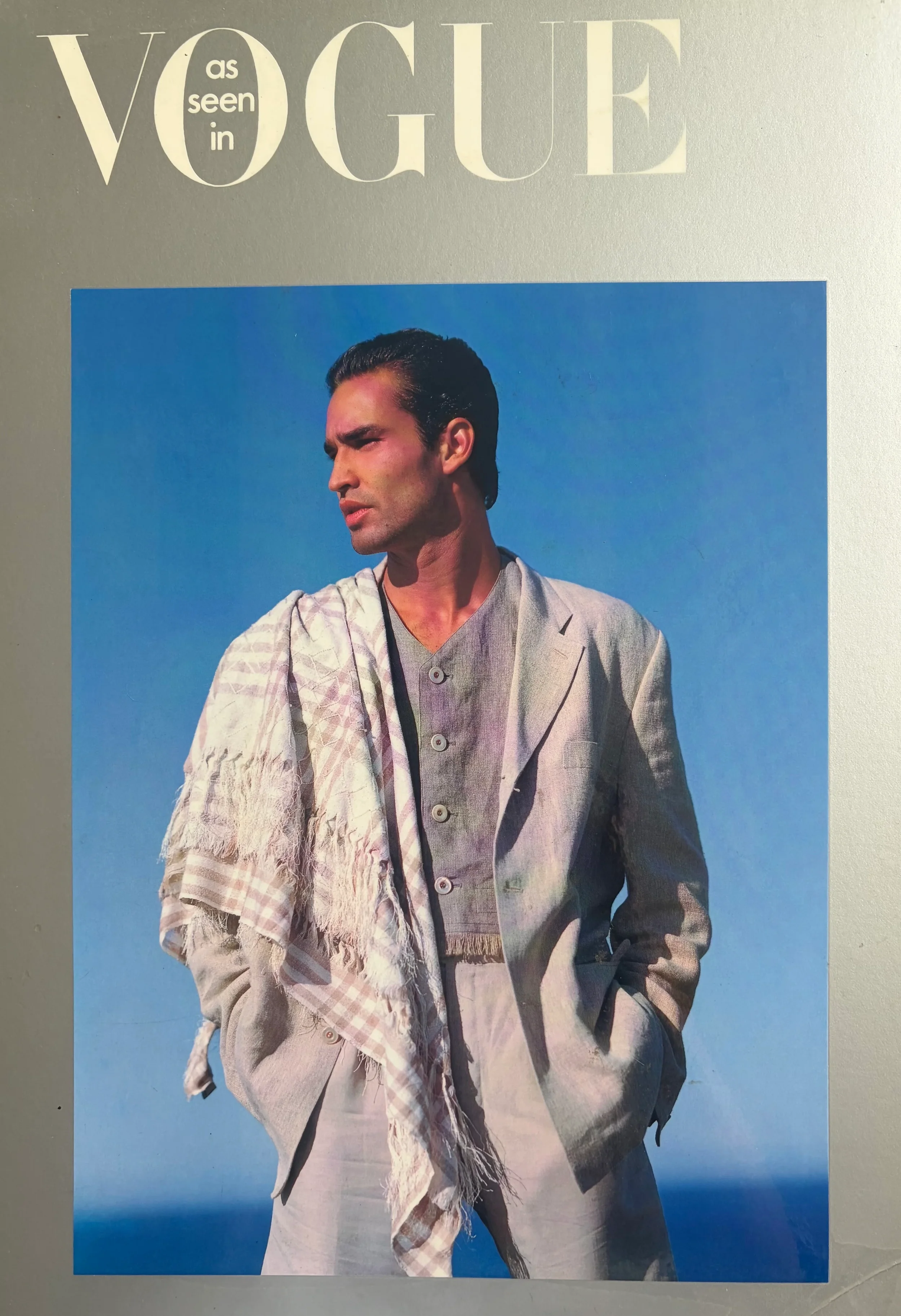 Cover of Vogue magazine featuring a man in a beige suit and shirt, with a plaid scarf draped over his shoulder, standing against a clear blue sky.