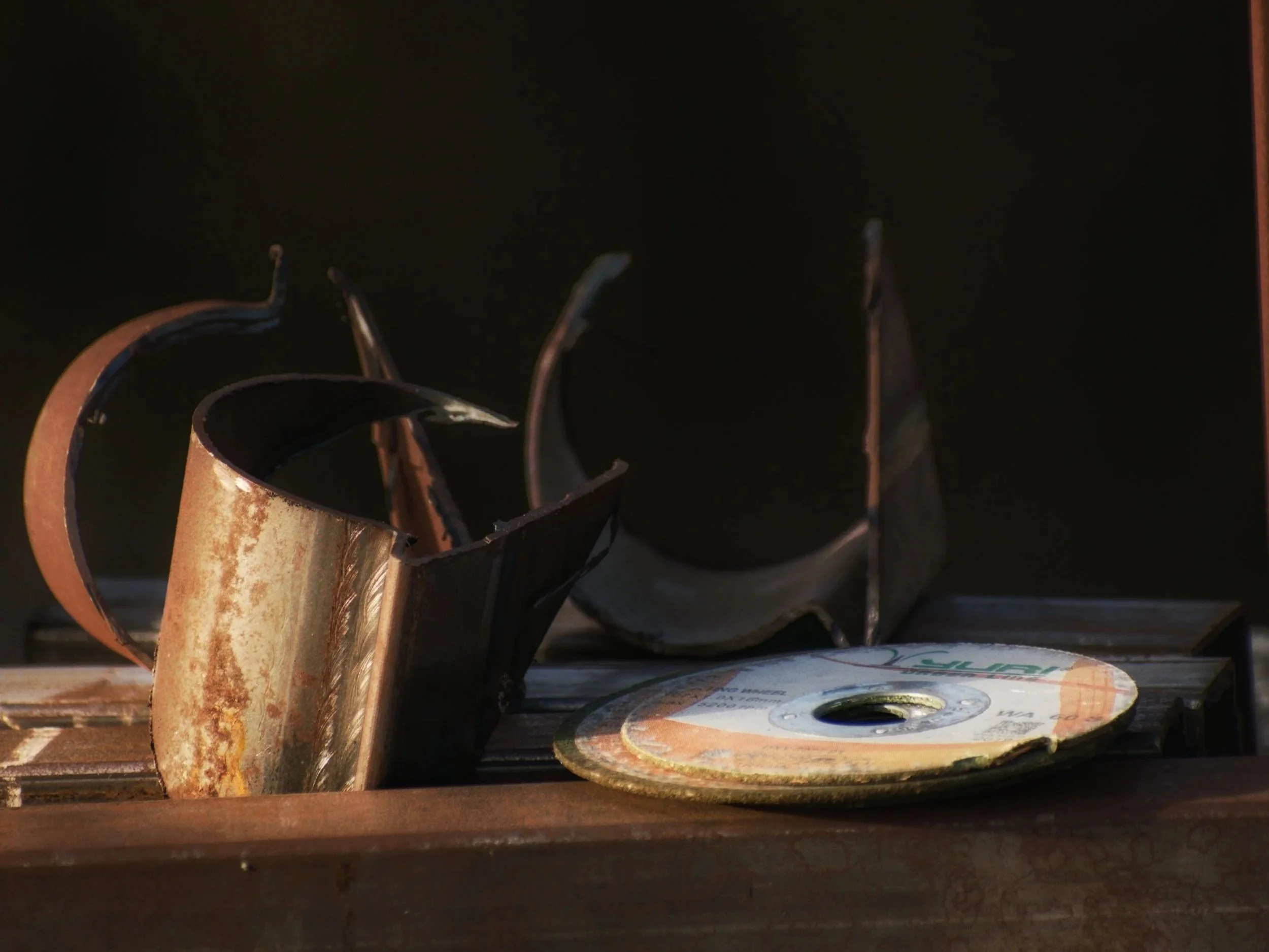 Close-up view of rusted metal pipe fittings with a spool of wire in the background on a wooden surface.