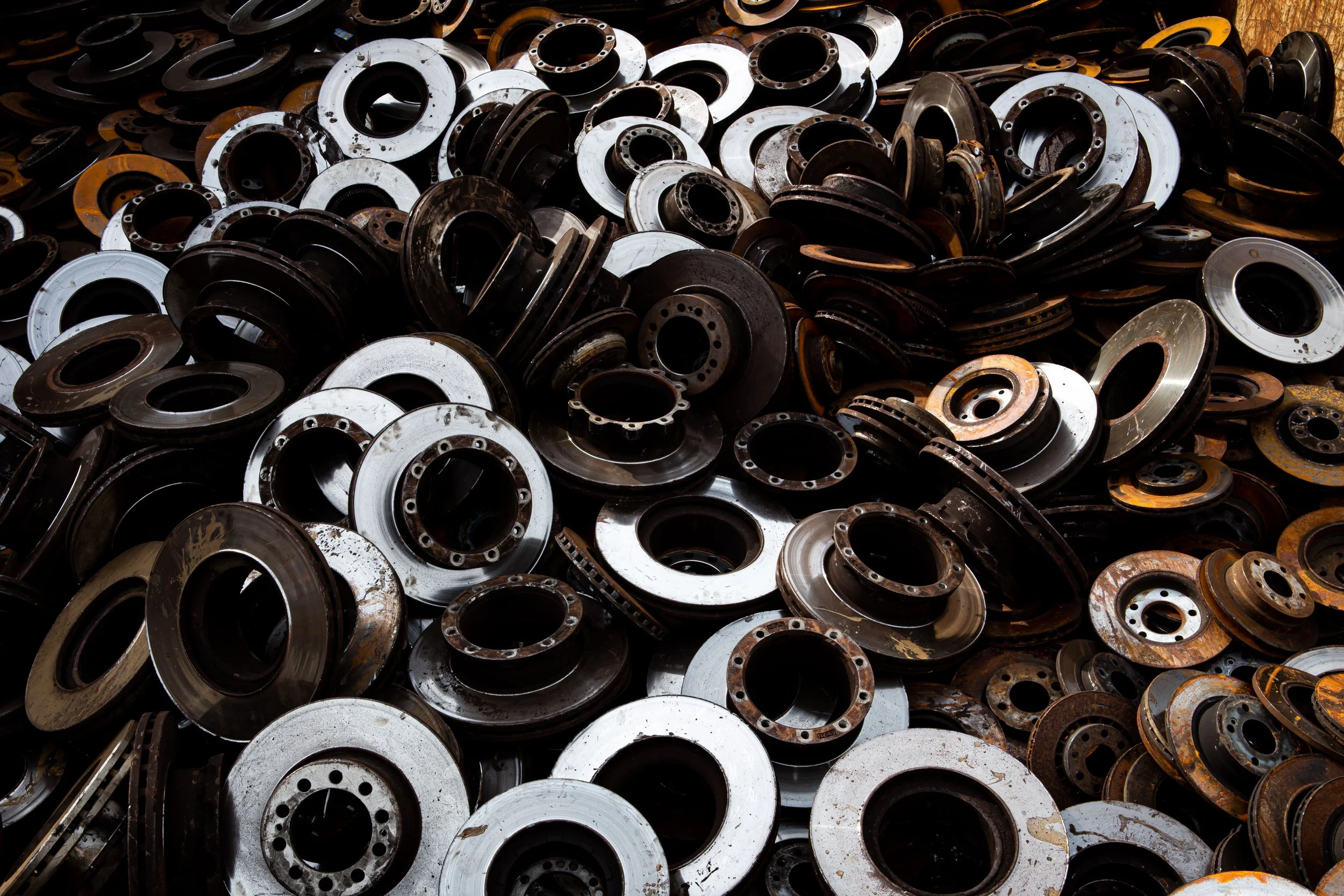 A large pile of metal machine parts, primarily circular flanges and disks, some with rust and dirt.