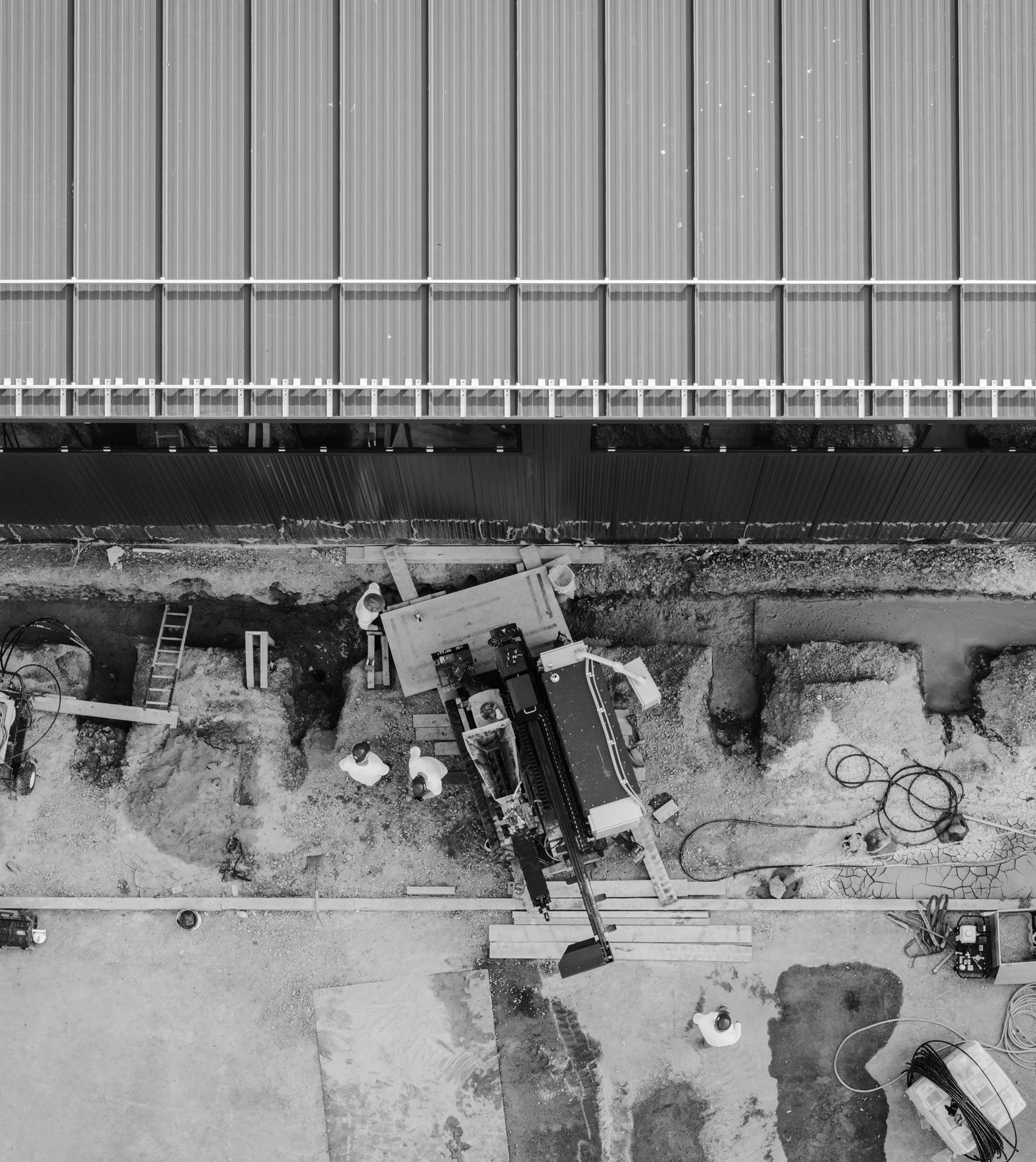 Drone image of DIG Energy construction workers wearing safety helmets and glasses installing a drill rig in front of a corrugated metal wall.