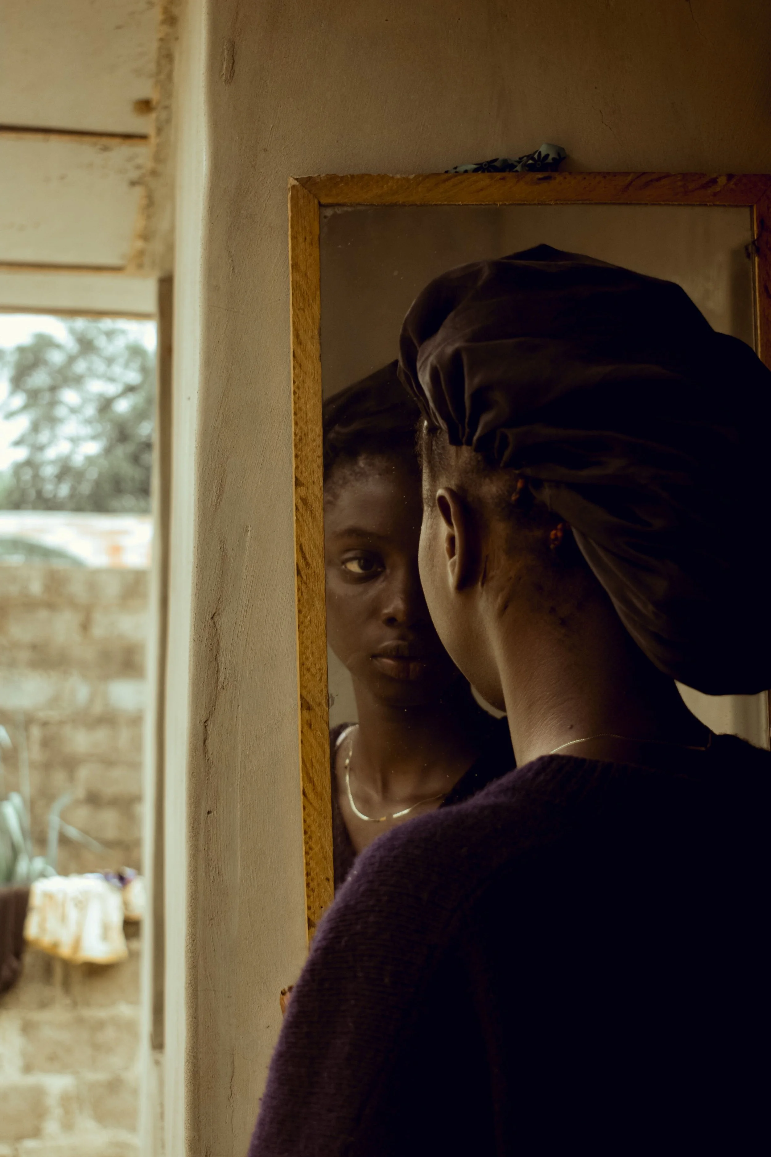 A woman is looking at herself in a mirror while another woman is helping or adjusting her hair.
