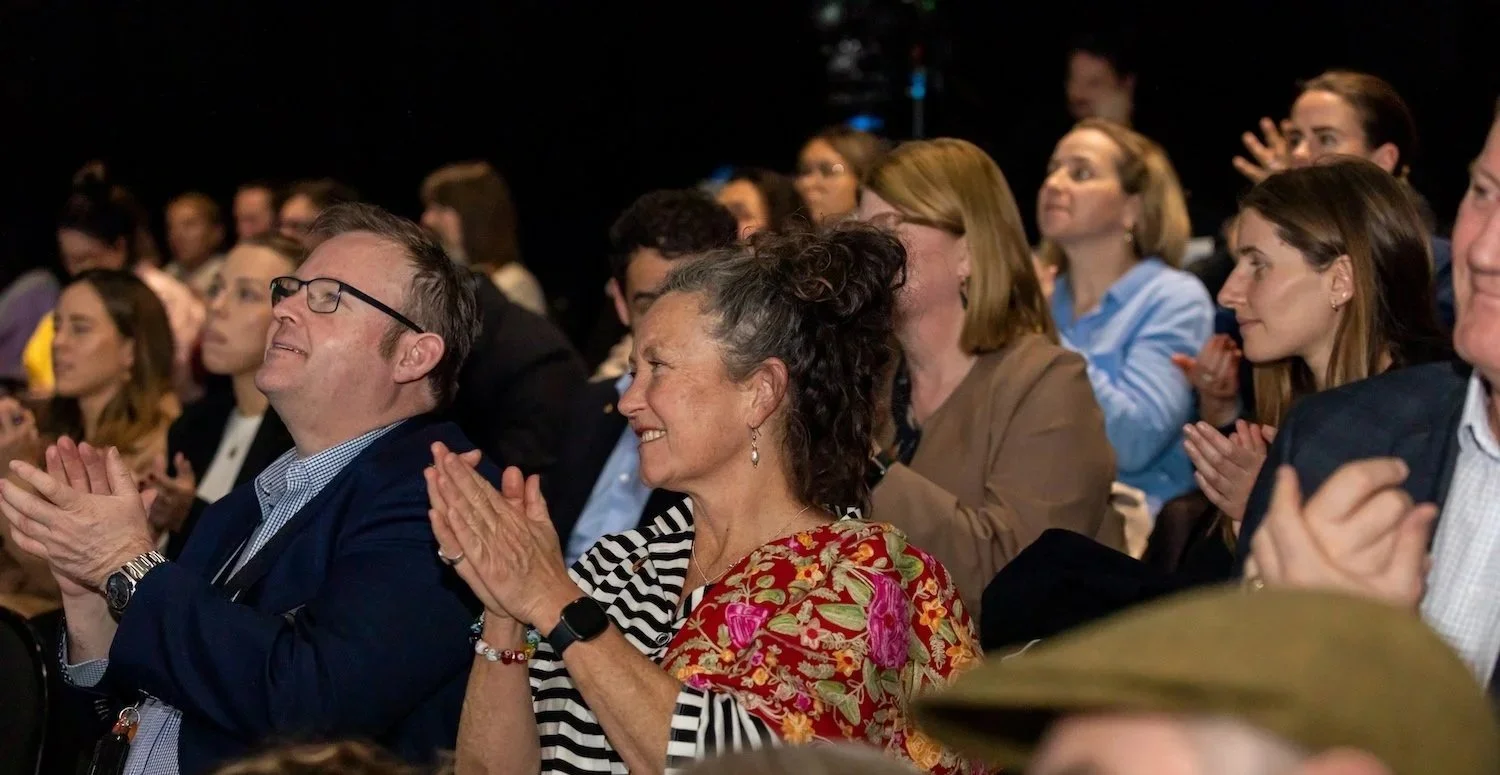 A group of people sitting in an audience, clapping and smiling at an event.