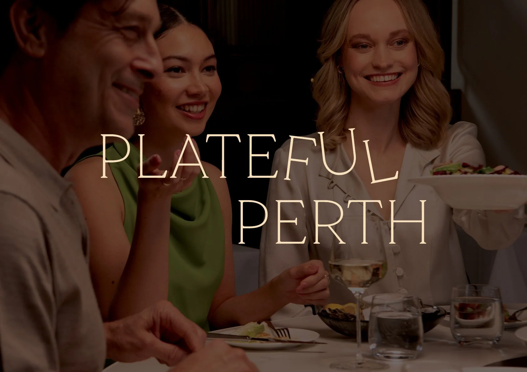 Four people sitting around a dining table, smiling and enjoying a meal in a dimly lit setting. One woman is holding a plate of salad, another has a glass of white wine, and there are various drinks and desserts on the table. The text overlay reads "P