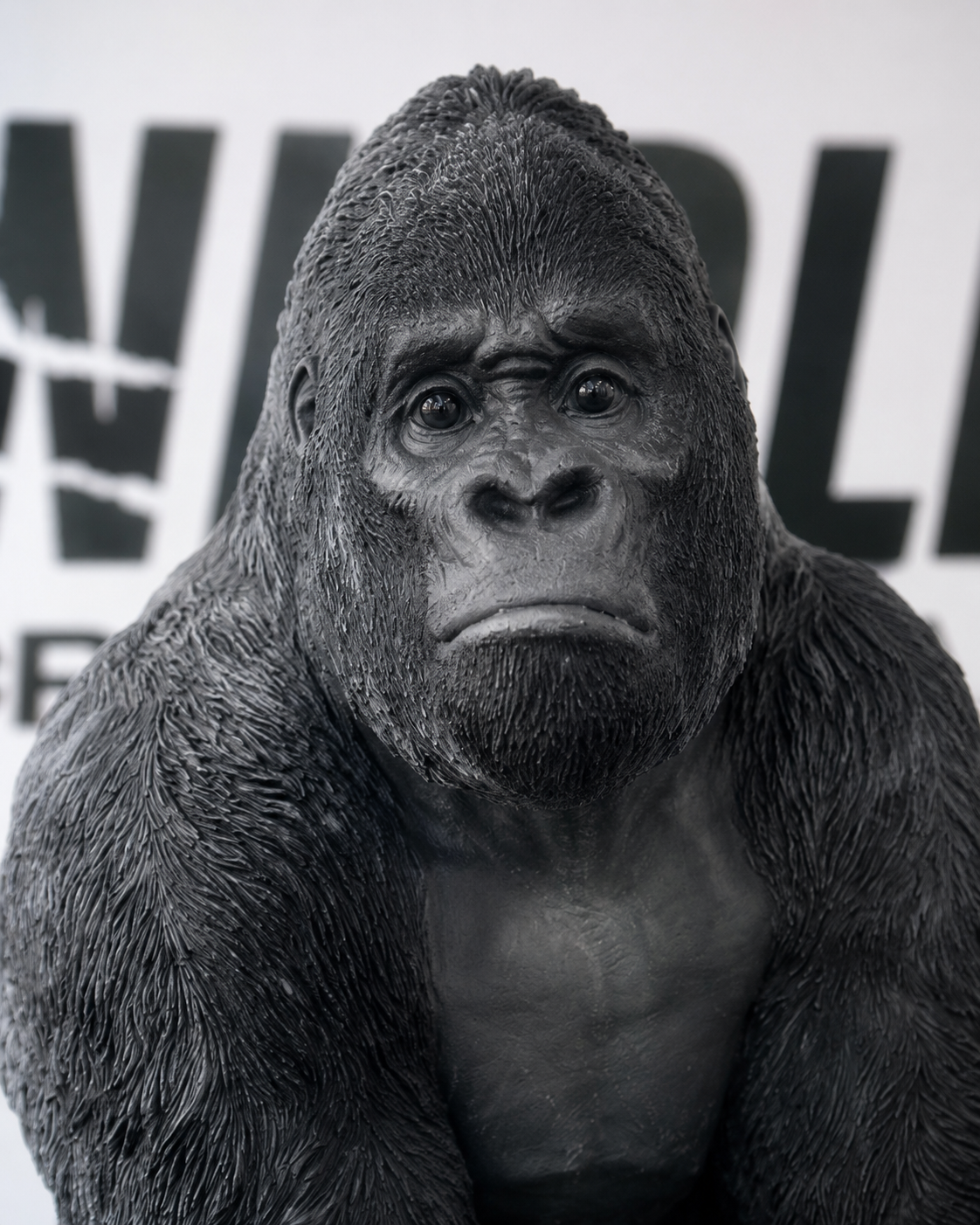 Close-up of a black gorilla statue with a serious expression, set against a blurred background with partial text