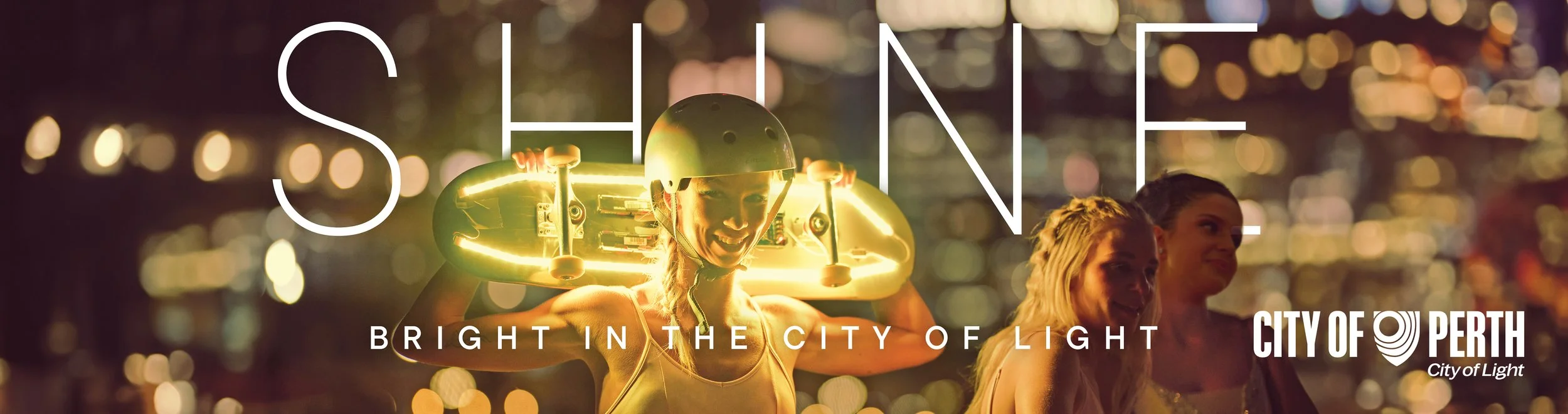 A woman wearing a helmet and holding a skateboard over her shoulders at night, with city lights in the background. The text reads 'SHINE' and 'Bright in the City of Light,' along with the City of Perth logo.