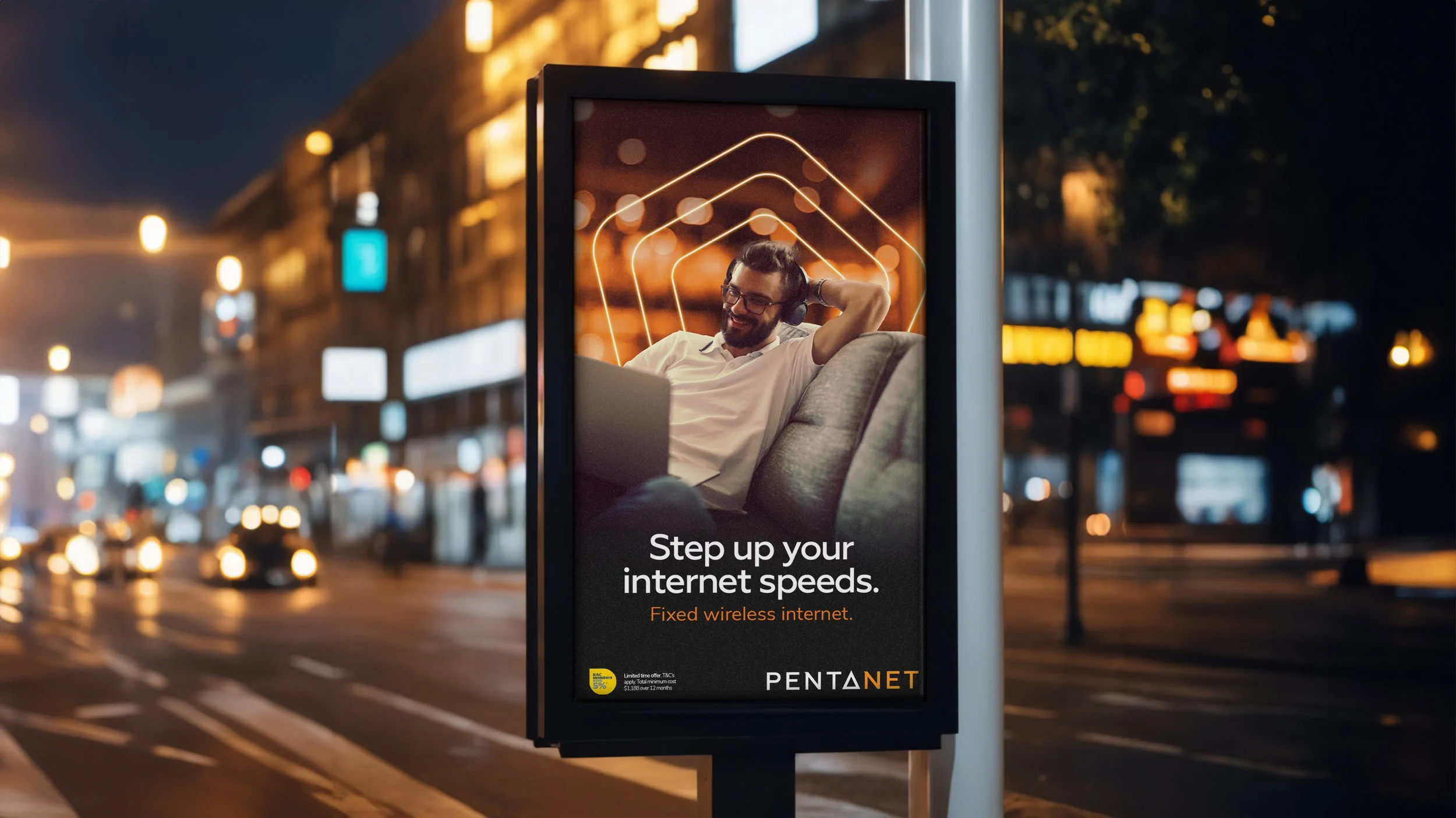 City street at night with a digital billboard promoting fixed wireless internet from PentaNet, showing a man wearing glasses and headphones, relaxing with a laptop, against a background of blurred city lights and traffic.