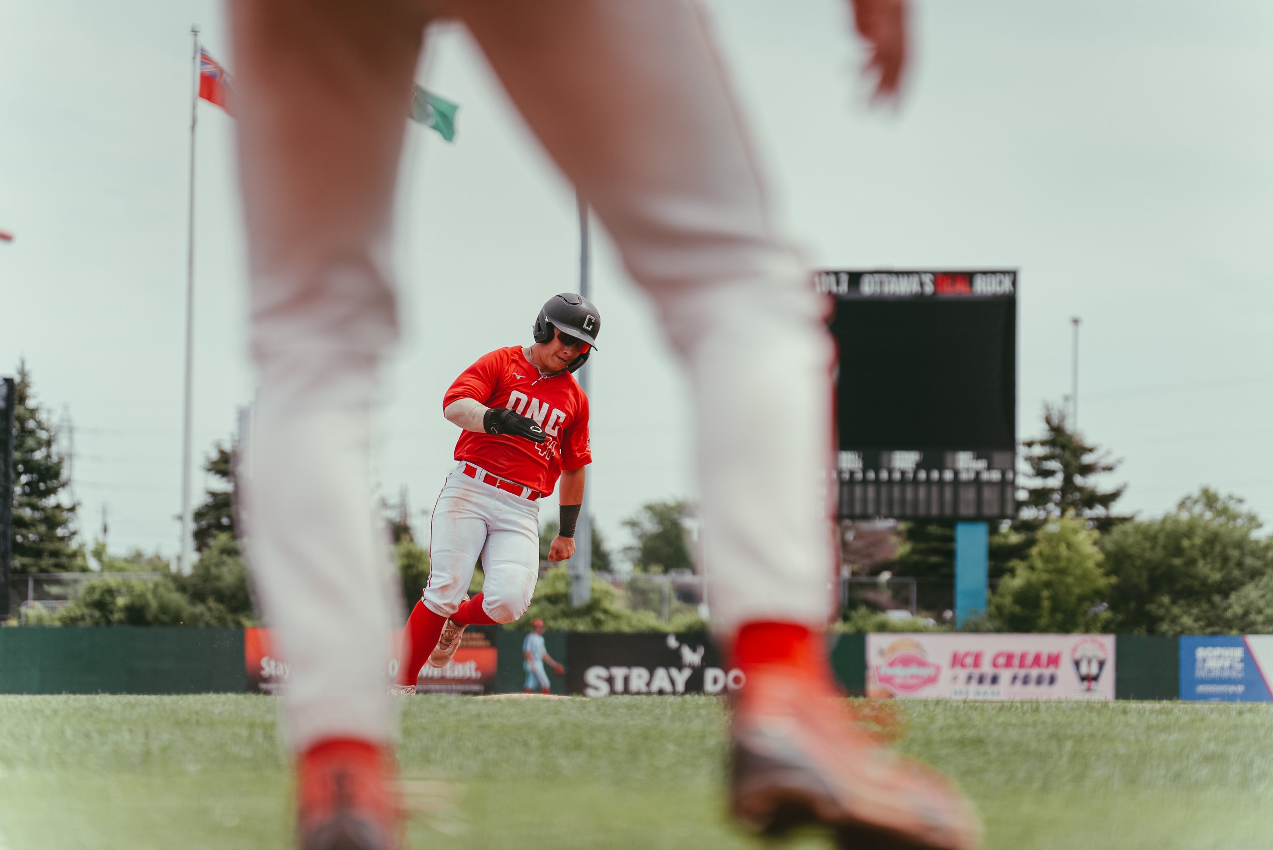A baseball player in a red uniform, wearing a helmet, is running the bases on a baseball field.