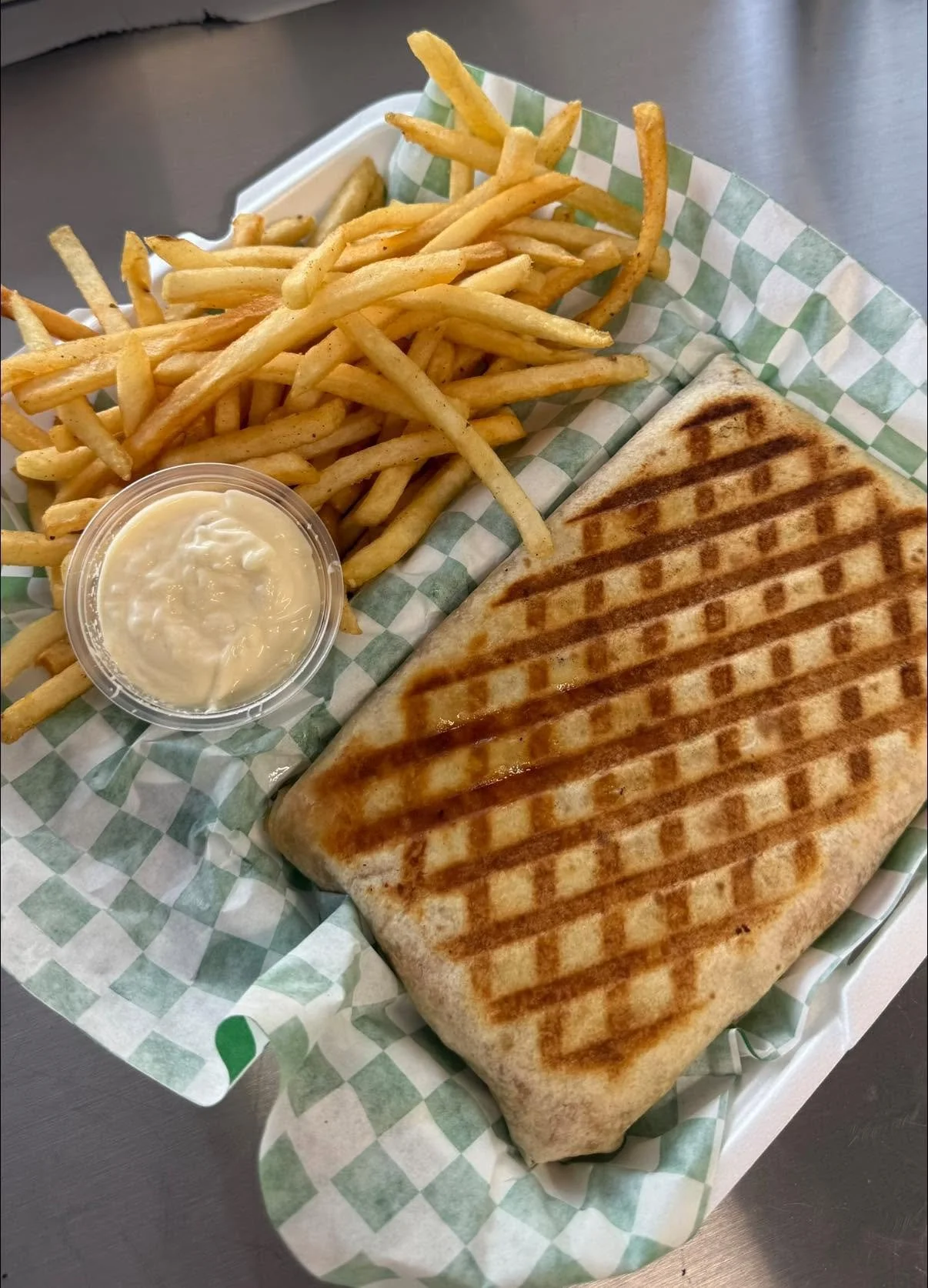 Grilled cheese sandwich with French fries and a small cup of dipping sauce on a checkered paper-lined tray.
