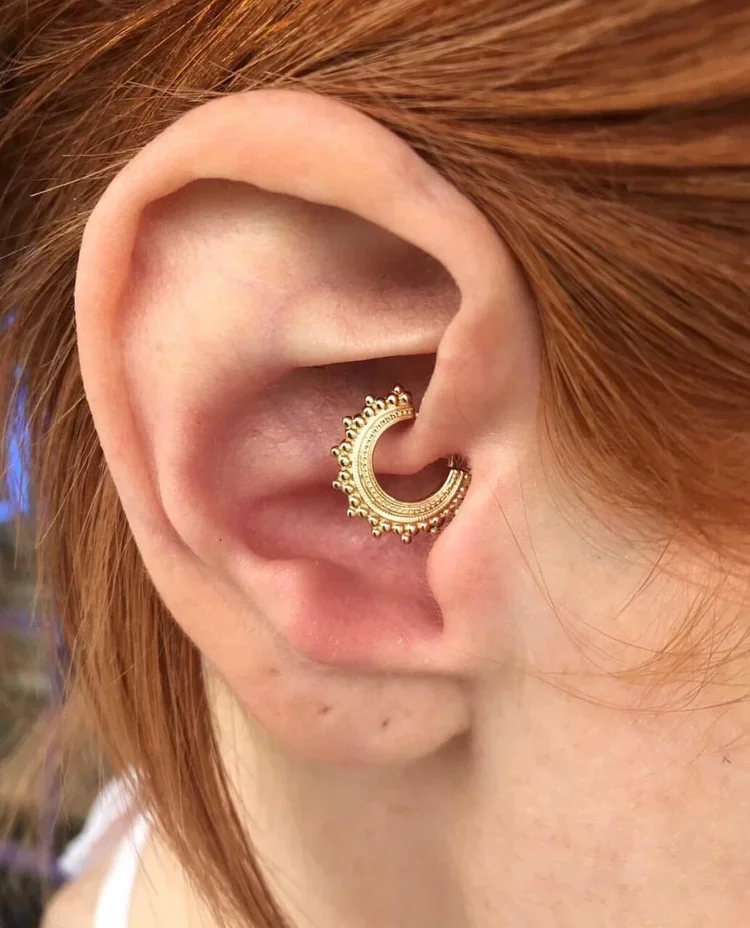 Close-up of a person's ear with a gold decorative hoop earring with a semi-circular design.