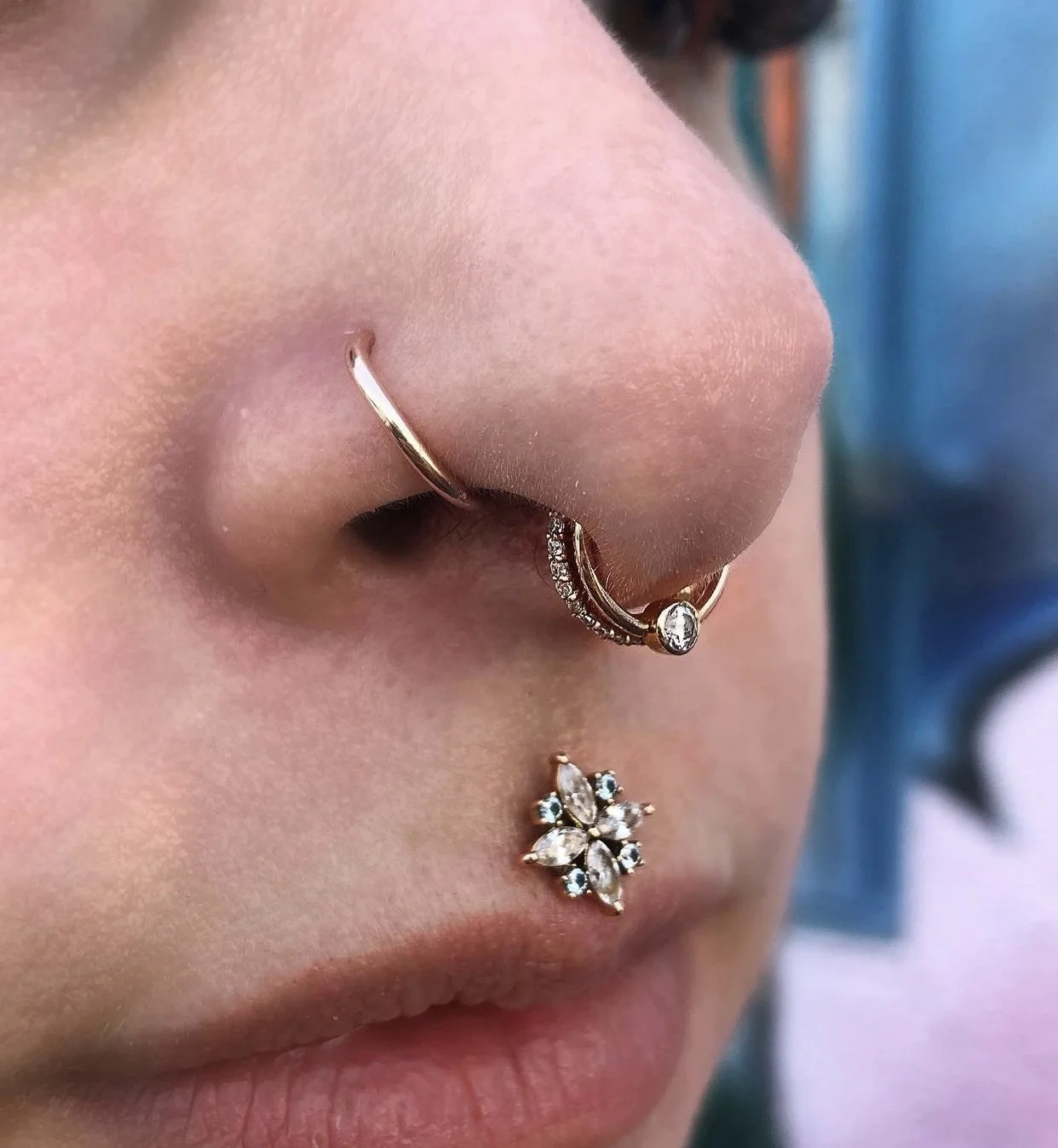 Close-up of a person’s face showing multiple facial piercings including a nose ring, a septum ring, and a lip ring, all adorned with small decorative stones.
