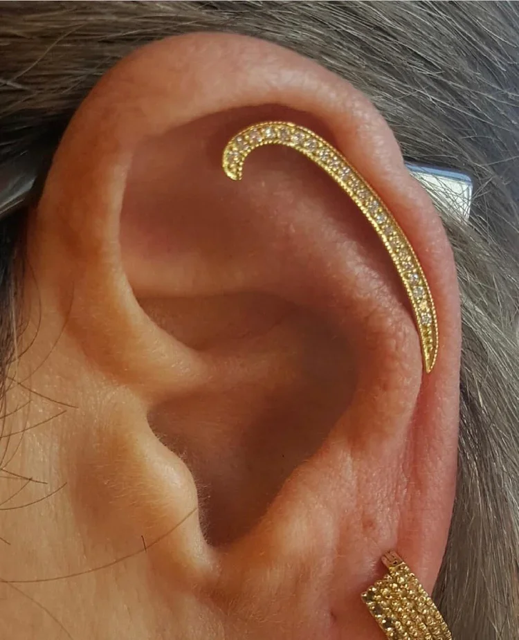 Close-up of a person's ear with a gold ear cuff and a gold earring, both decorated with small diamonds.