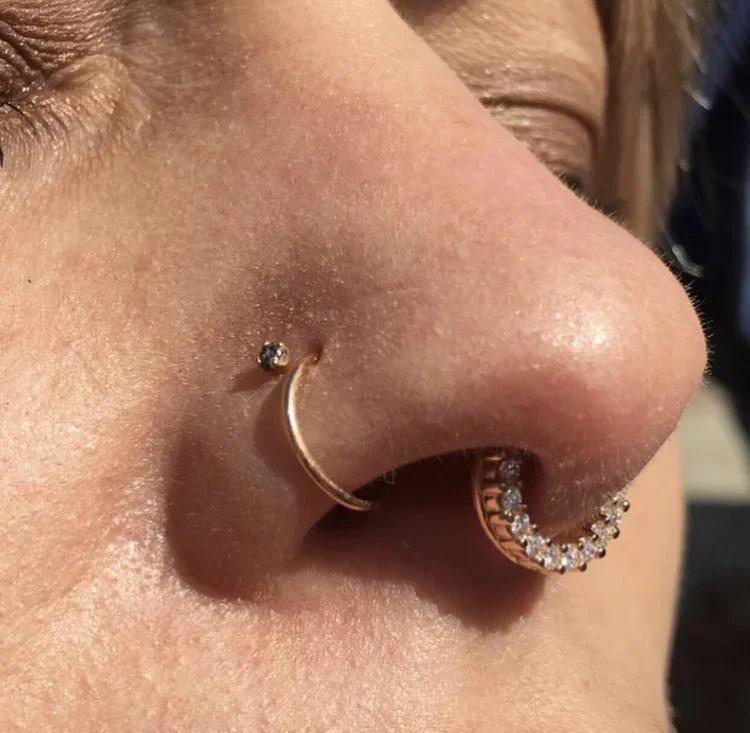 Close-up of a person's nose with two nose rings, one with small diamonds and the other a plain hoop, and visible skin texture.