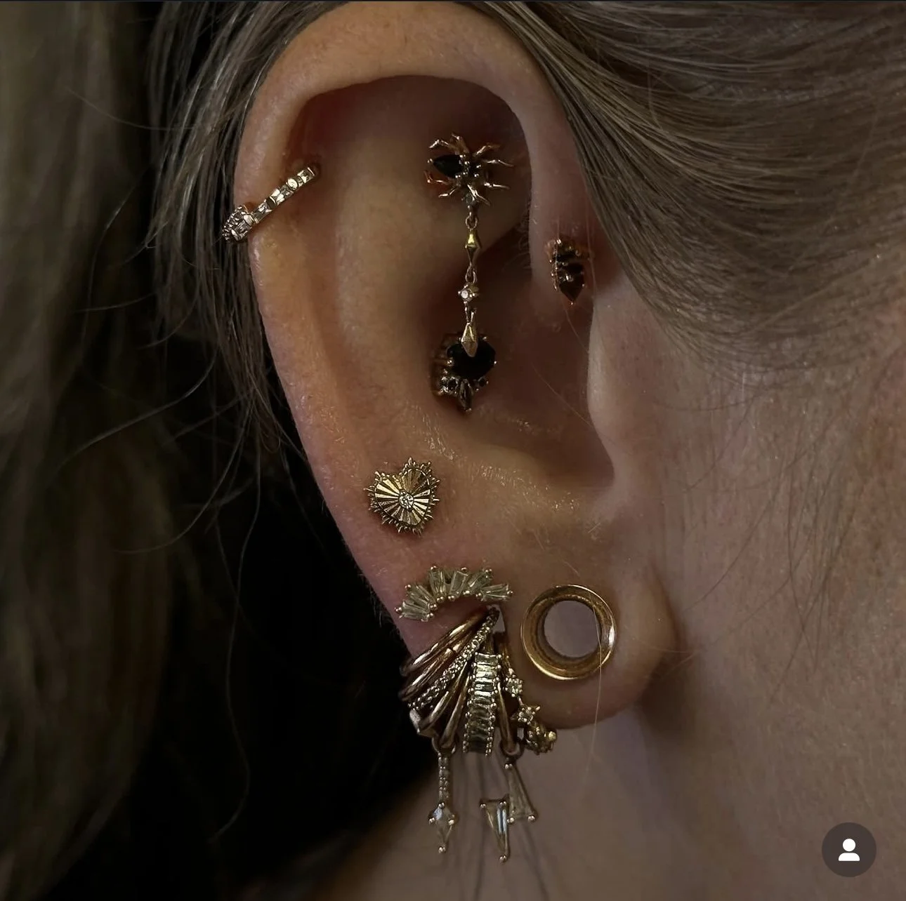Close-up of a person's ear with multiple gold and silver earrings, including hoops, studs, and dangling designs.