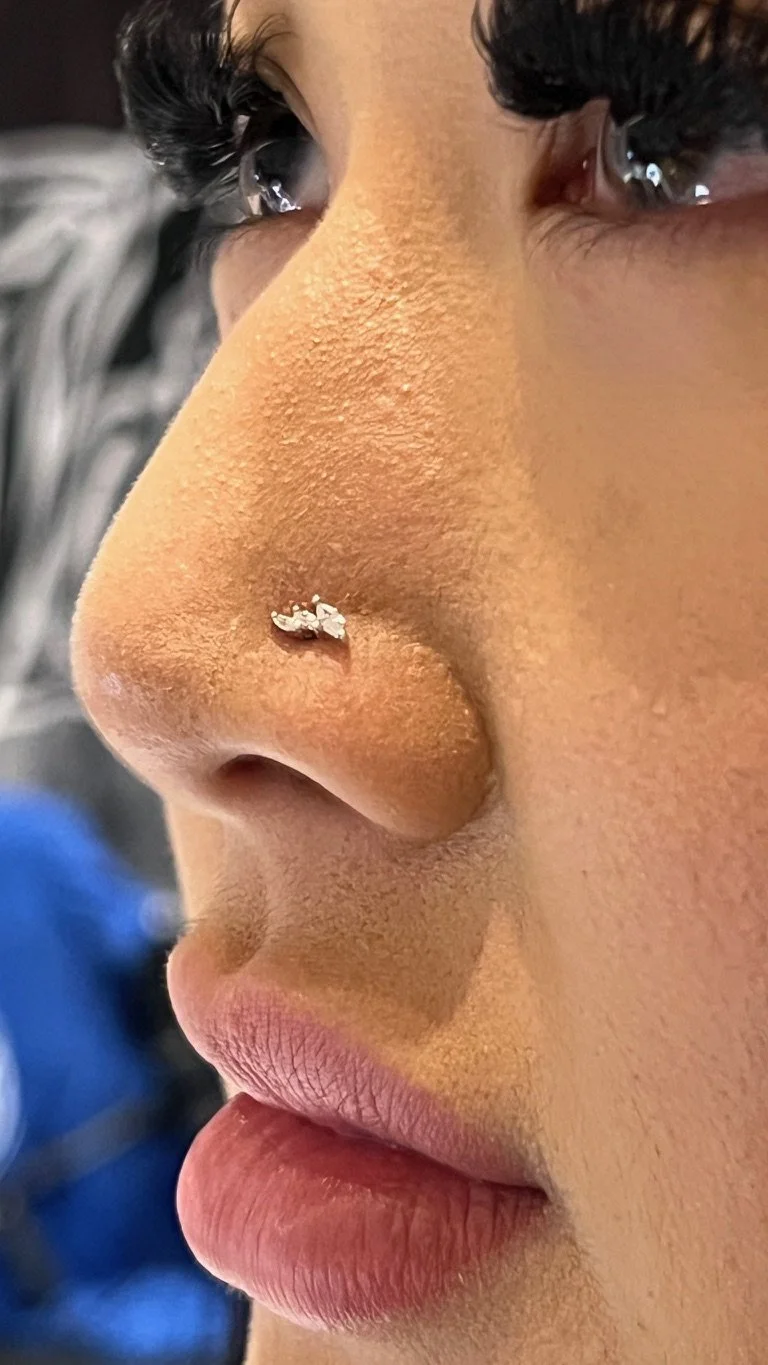 A close-up of a person's face, showing the nose with a small nose ring, lips, and dark, curled eyelashes.