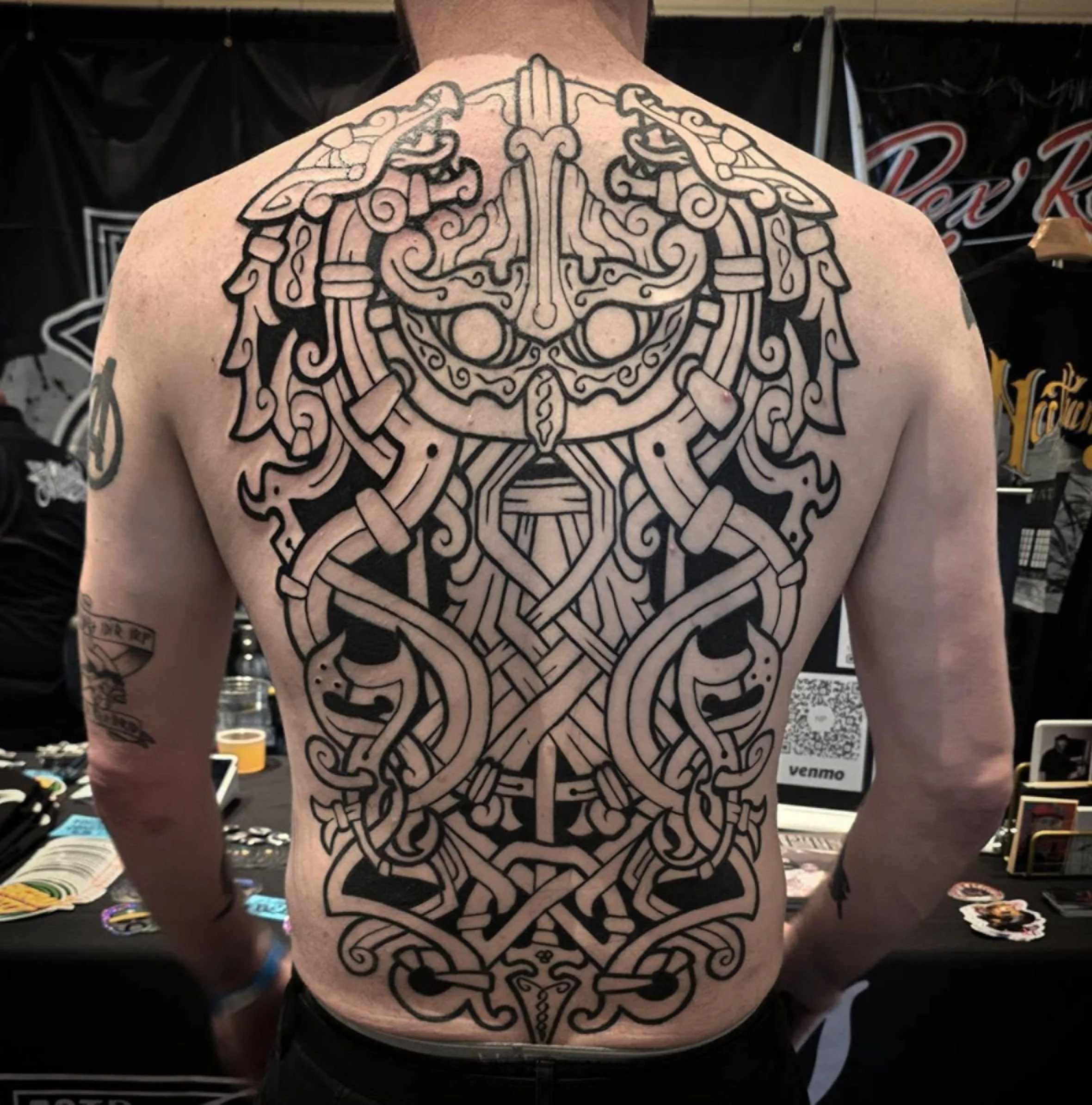 Back tattoo of an intricate tribal design, resembling a stylized animal face, on a person's upper back and shoulders.
