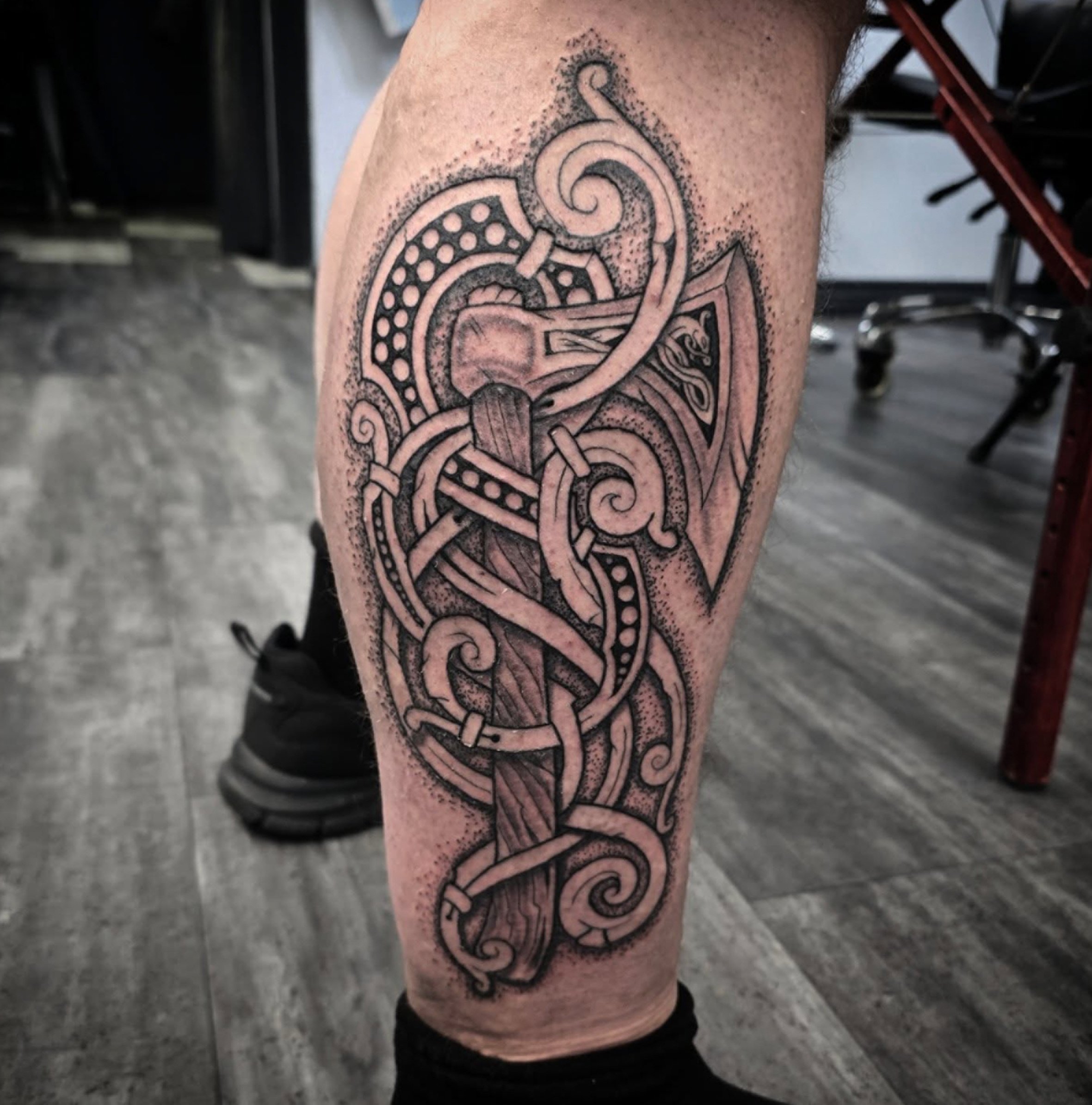 Close-up of a person's arm with a large, intricate black ink tattoo featuring swirling Celtic knot designs and dot shading.