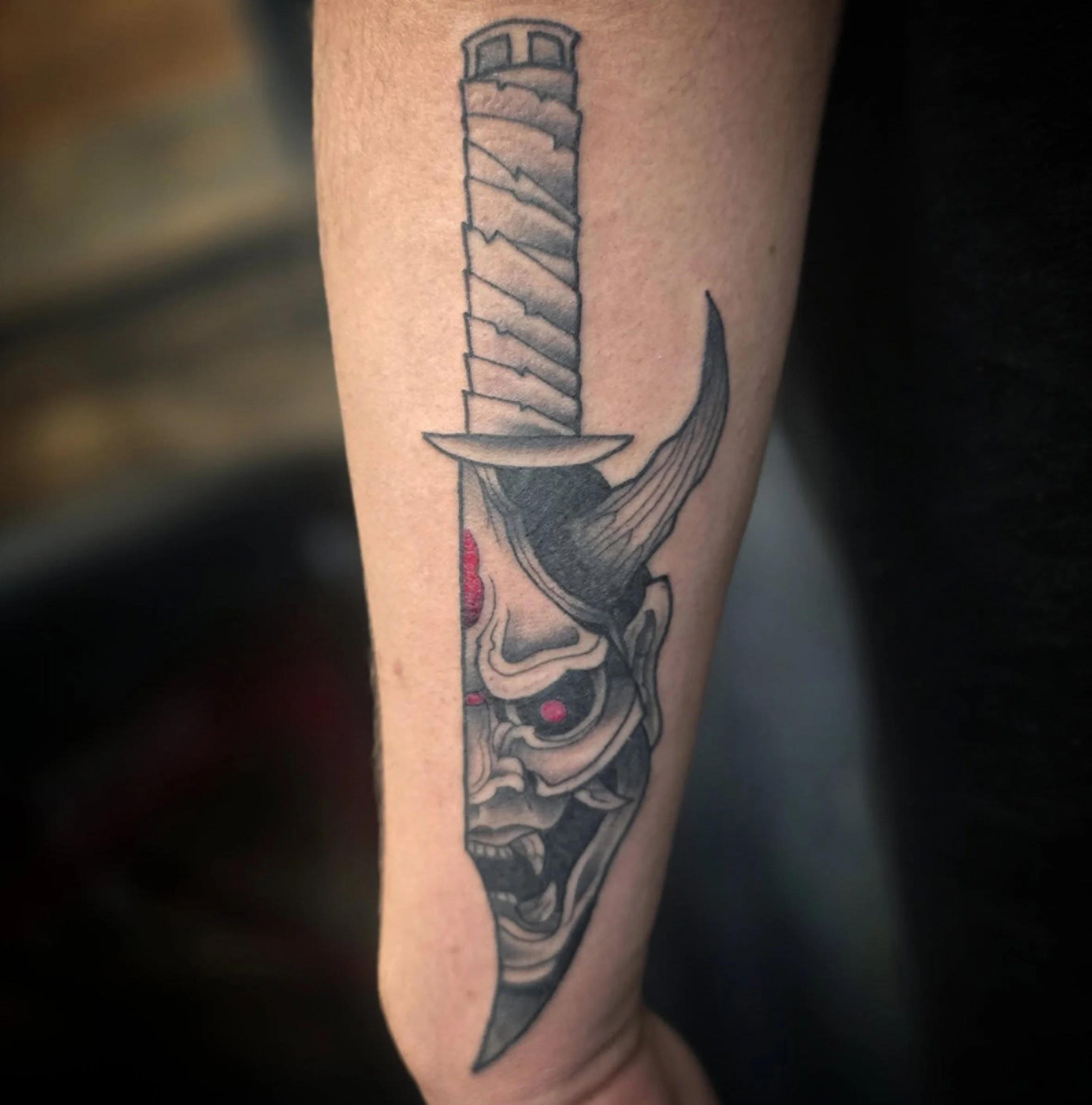A tattoo of a sword on a person's upper arm with black and gray shading.