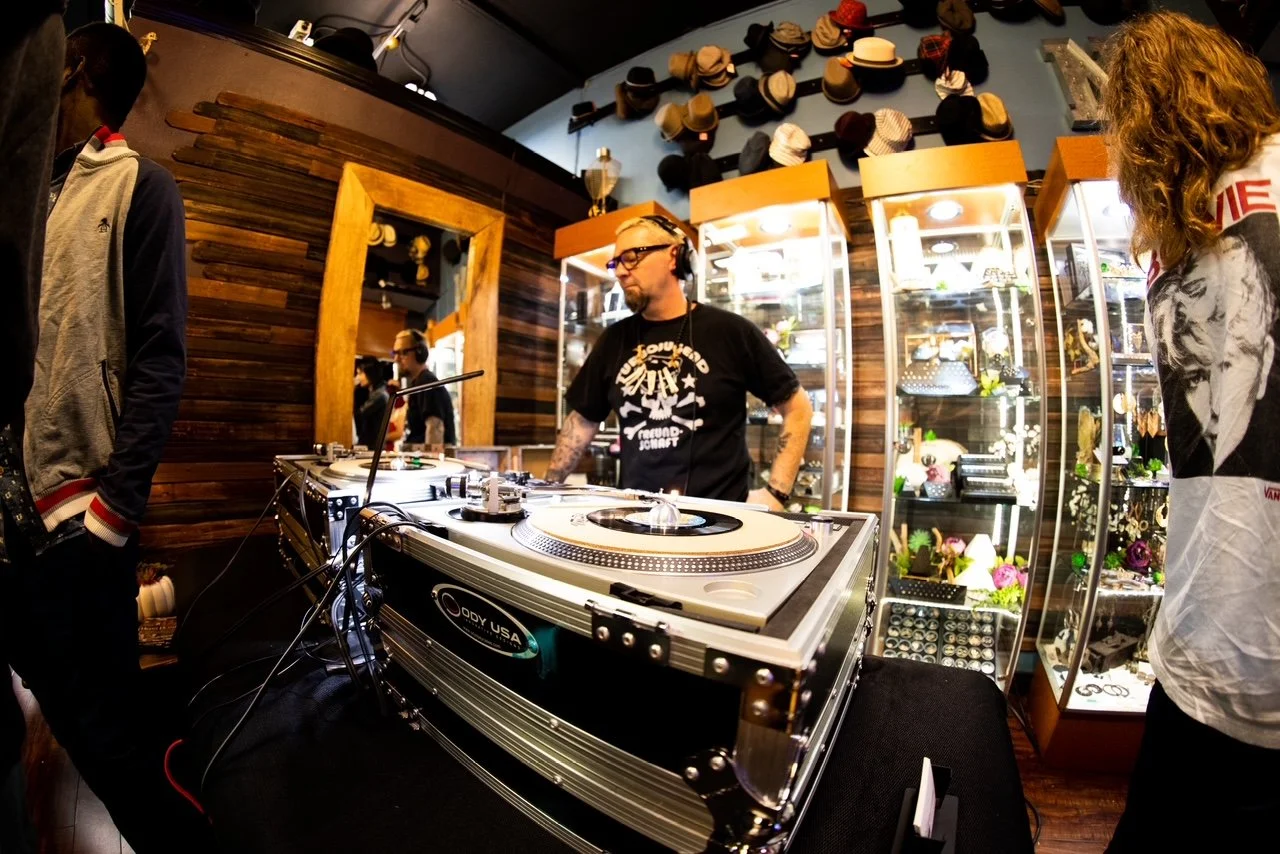DJ playing music at a turntable setup in a boutique store with shelves of accessories and hats.