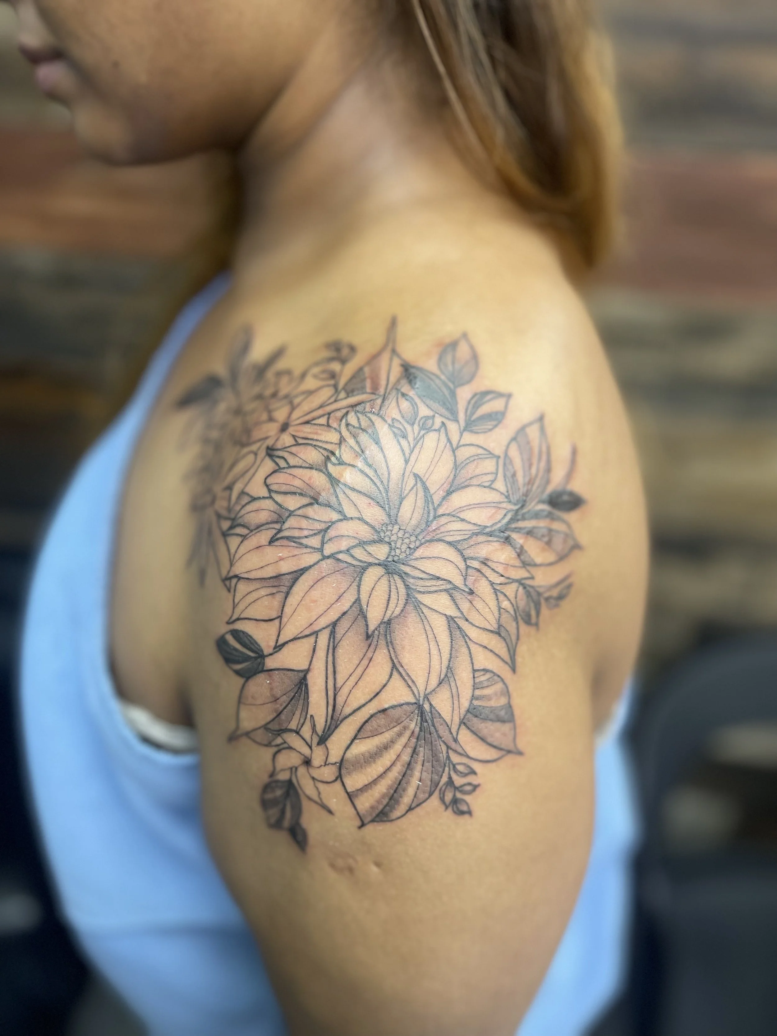 Close-up of a woman's upper arm with a floral tattoo featuring large flowers and leaves.