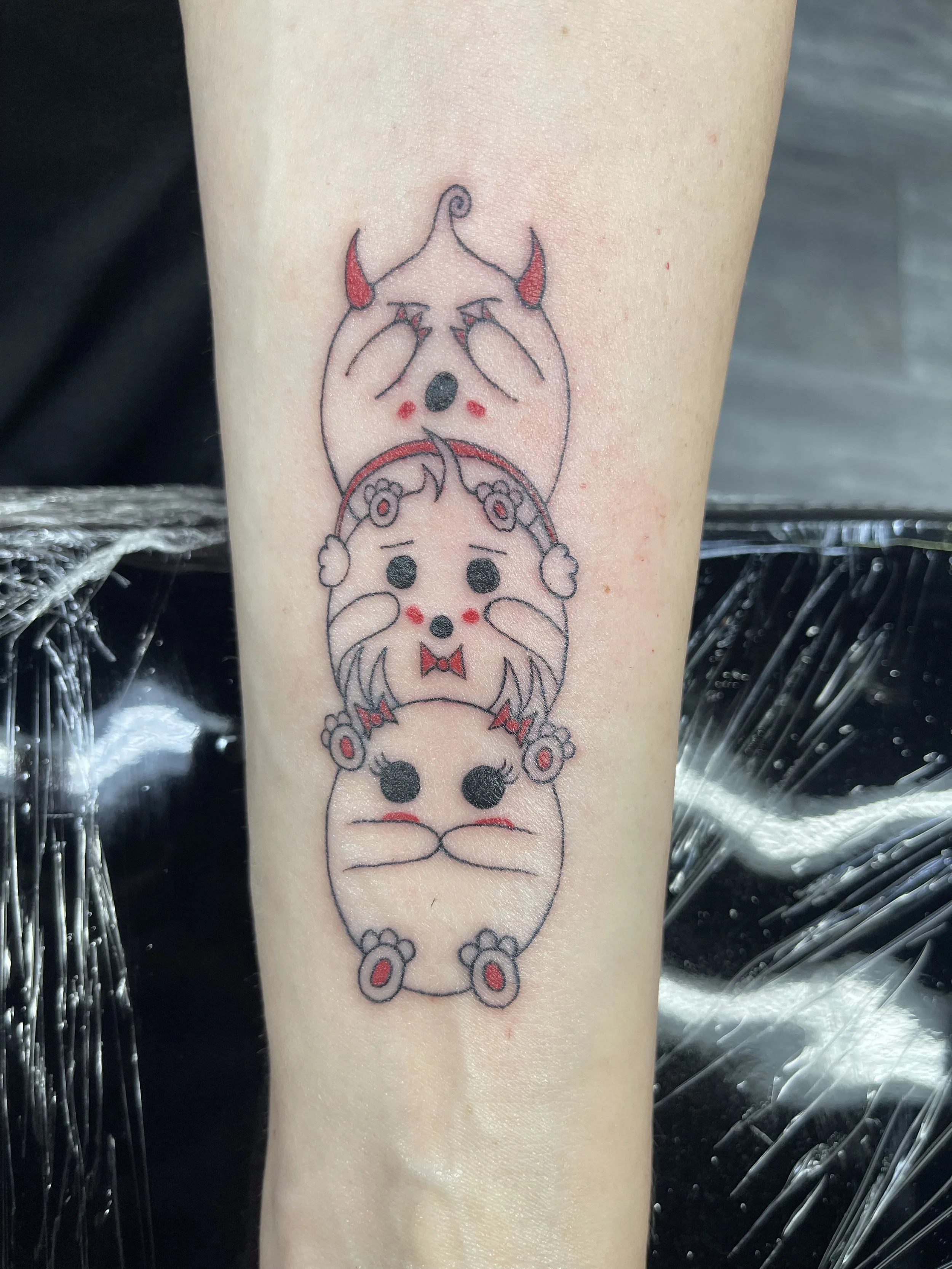 Tattoo of a cute cartoon dog with a gray body, black nose, red cheeks, and red ears and paws, sitting upright.