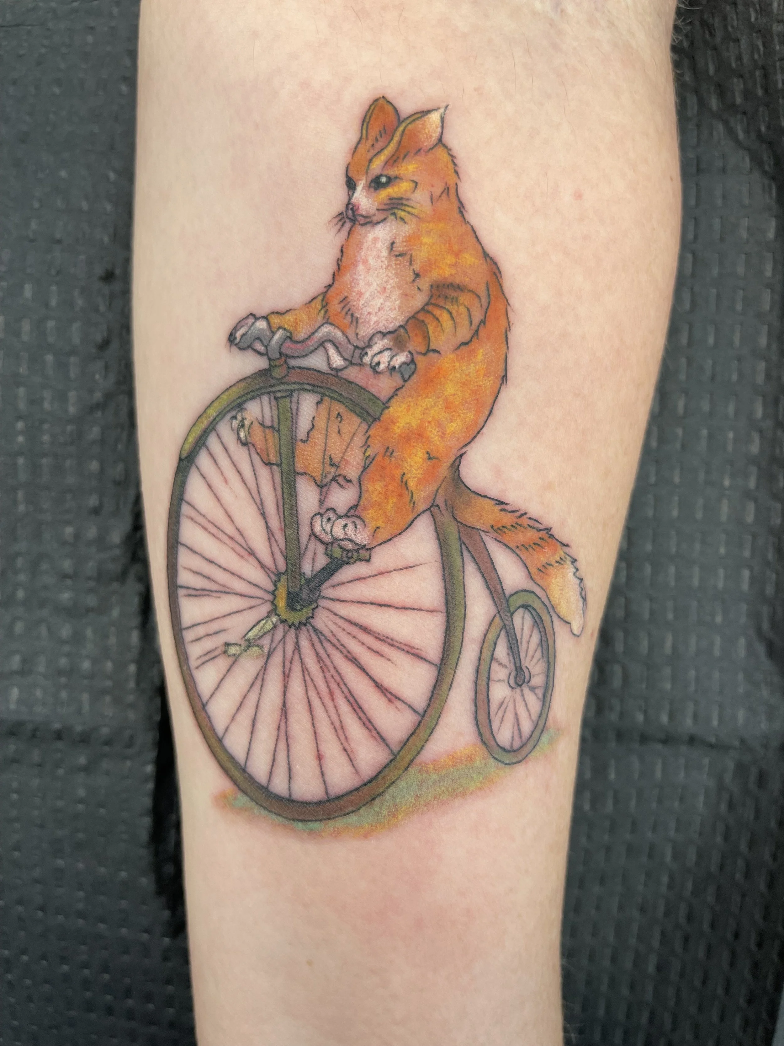 Tattoo of a fox riding a bicycle, with the front wheel of the bike replacing the fox's body.