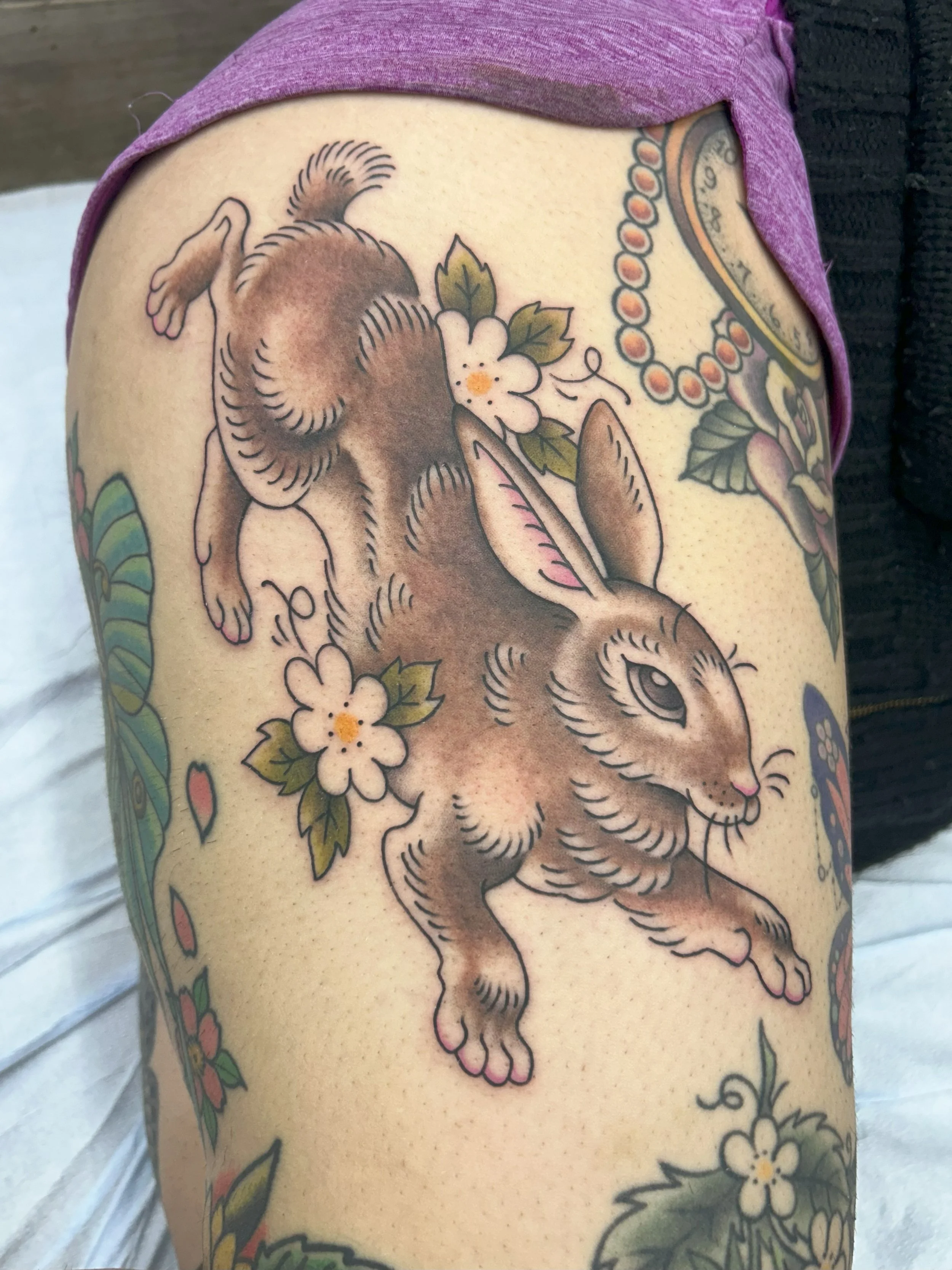Colorful tattoo of a crouching dog with flowers and a clock on the shoulder.
