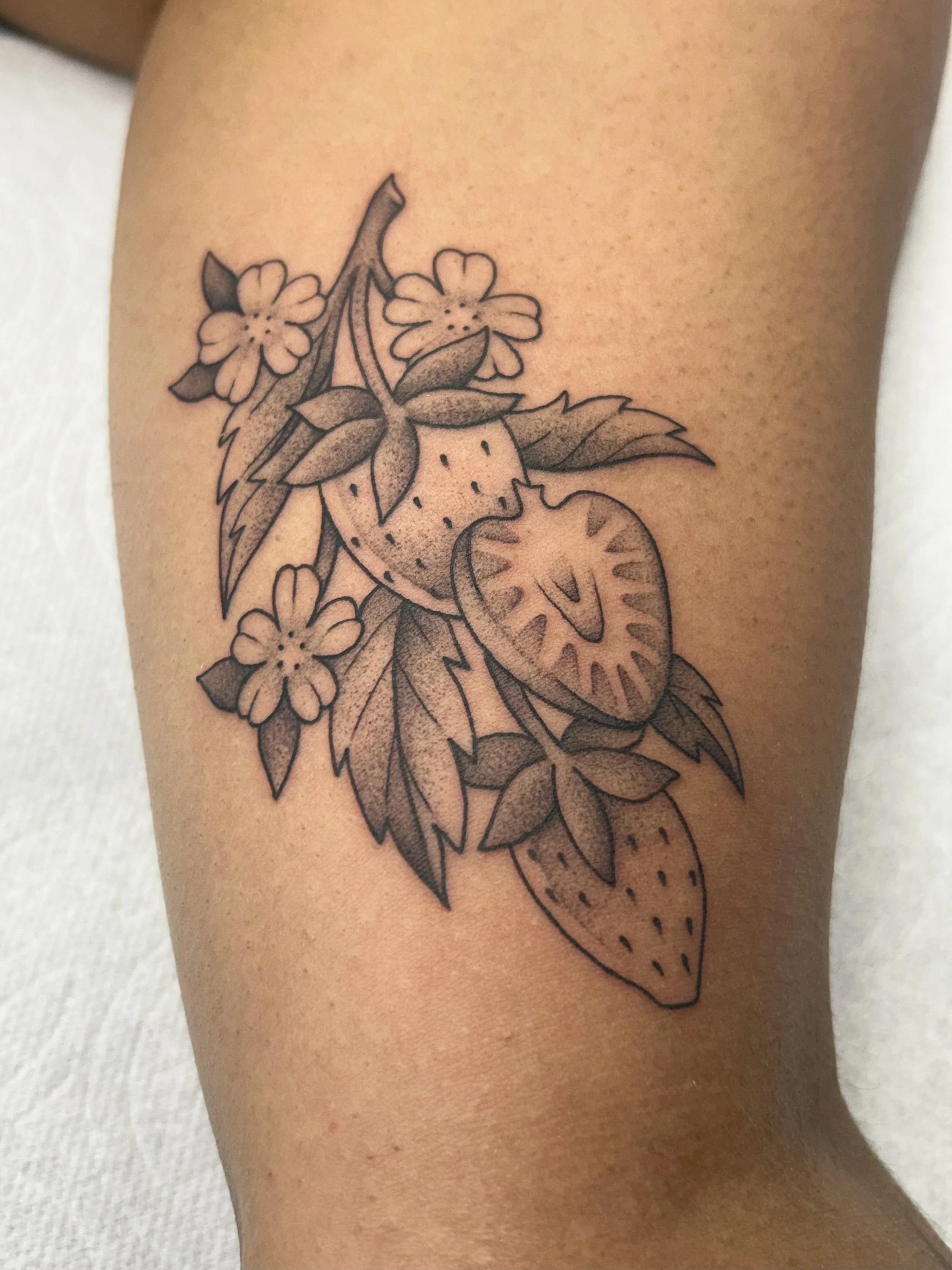 A tattoo of strawberries, leaves, and flowers on a person's arm.