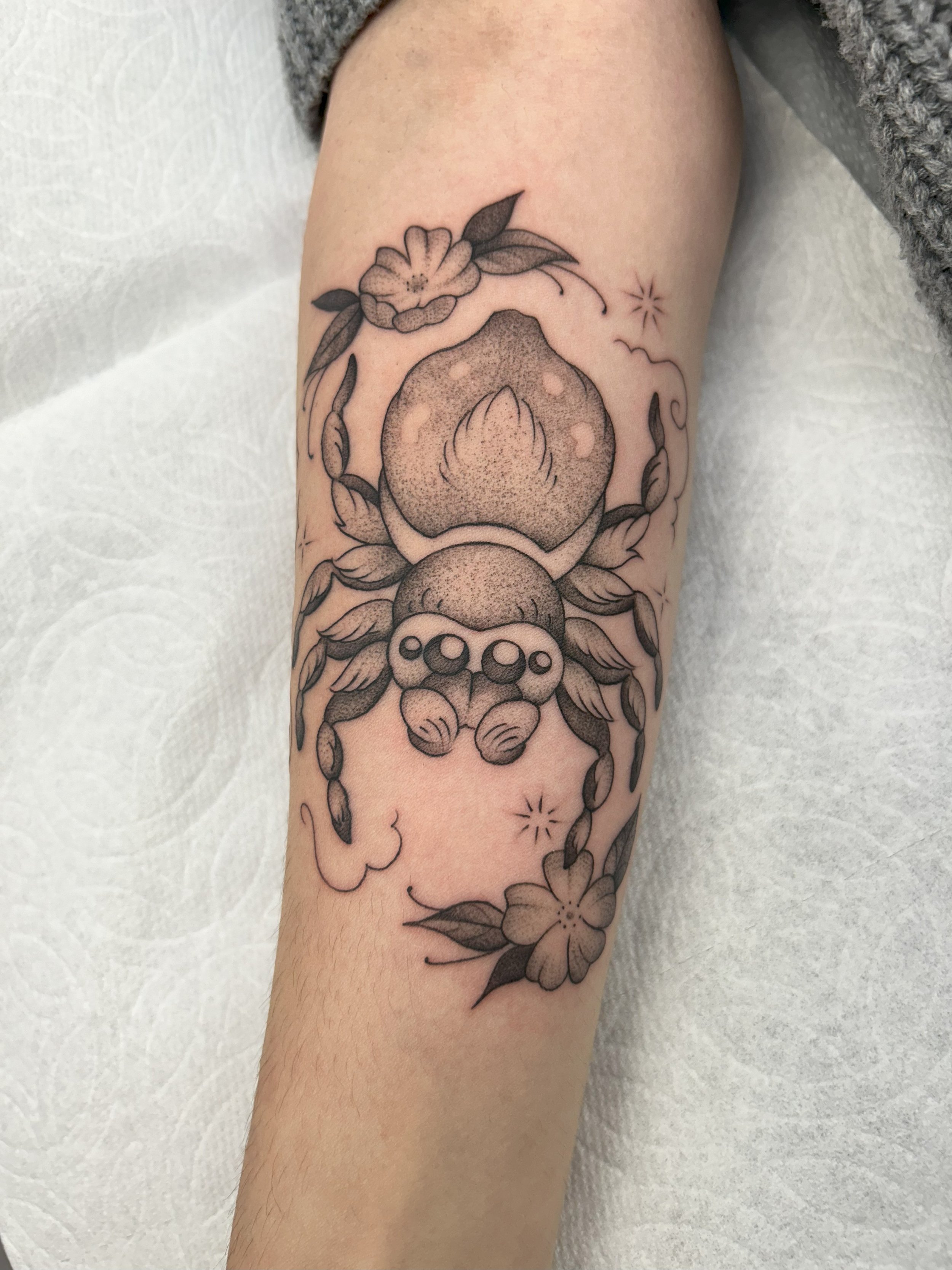 Tattoo of a peach surrounded by flowers and leaves on a person's forearm.