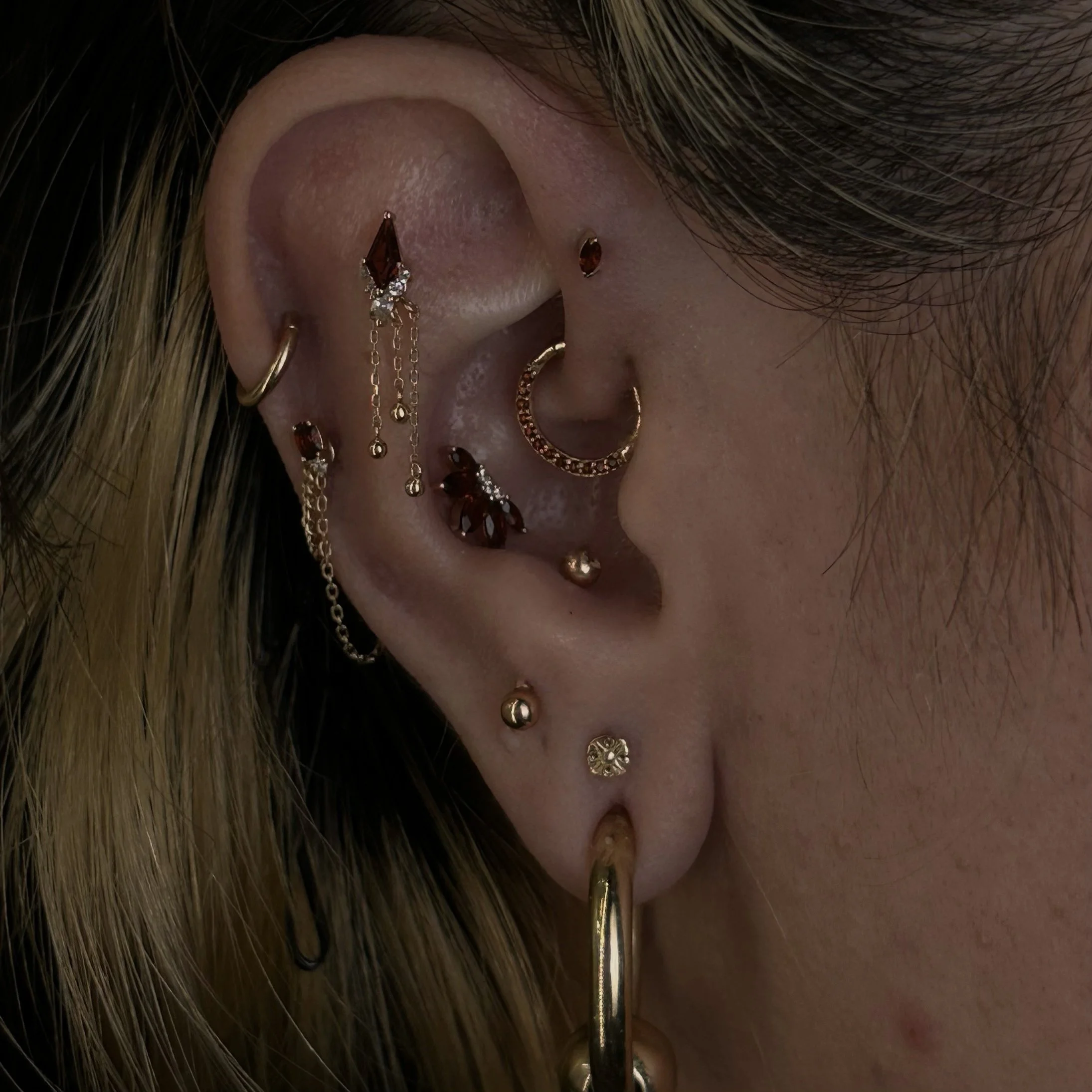 Close-up of a person's ear decorated with multiple gold earrings and a chain earring, with their hair partially covering the area.