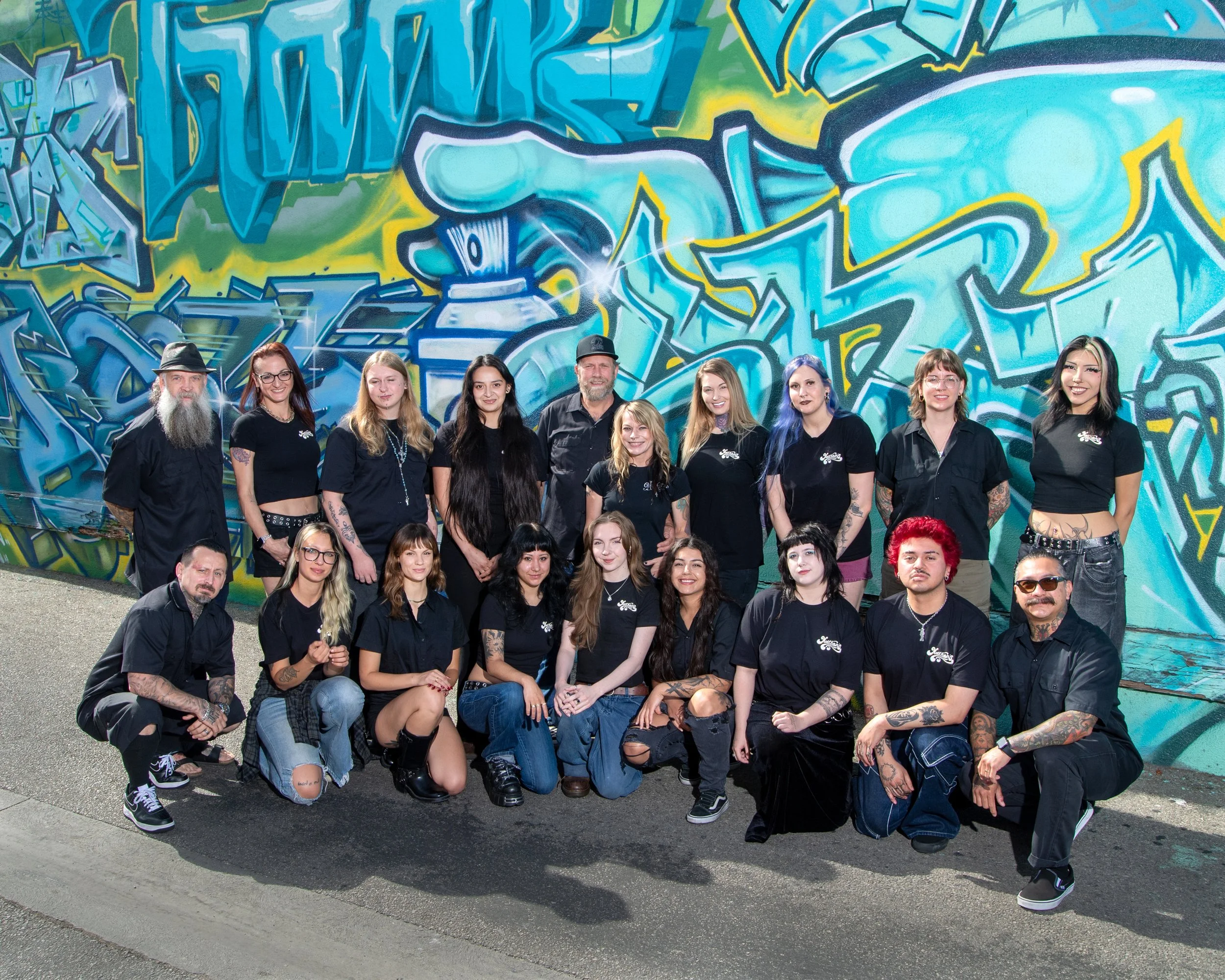 A group of diverse people posing in front of a colorful graffiti wall with blue, green, and yellow designs.