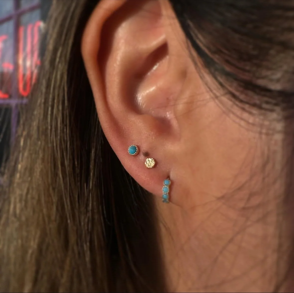 Close-up of a woman's ear with three piercings, each adorned with various small, colorful earrings.