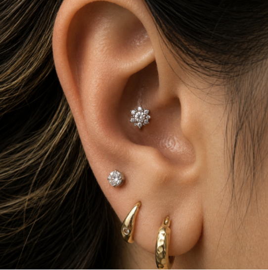 Close-up of a person's ear with multiple earrings, including a small stud, a tiny snowflake-shaped earring, and two gold hoops.