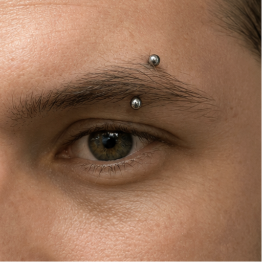 Close-up of a person's eye with two silver eyebrow piercings.