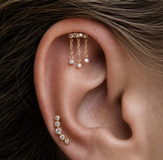Close-up of a woman's ear with multiple earrings, including a gold chain with three dangling diamonds and a small gold hoop with three diamonds.