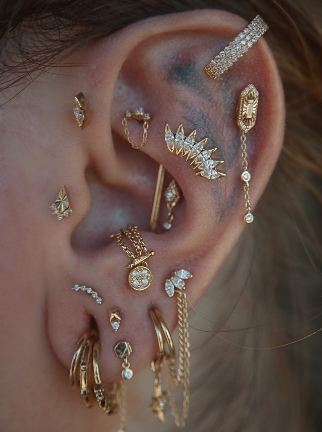 Close-up of a person's ear decorated with multiple gold and diamond-studded earrings in various designs.